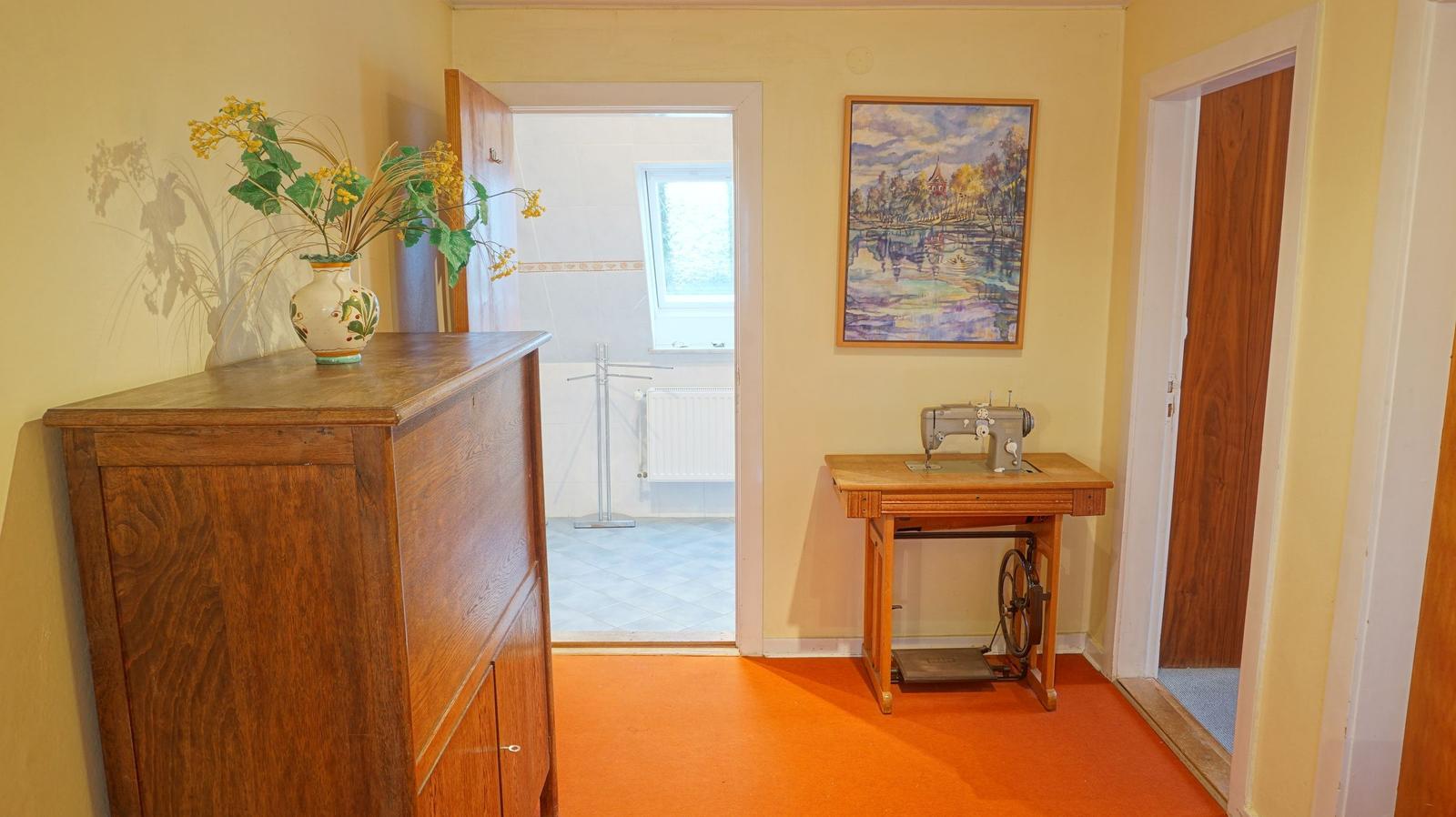 Hausflur mit Holzschrank, Nähmaschine und Bild an der Wand.