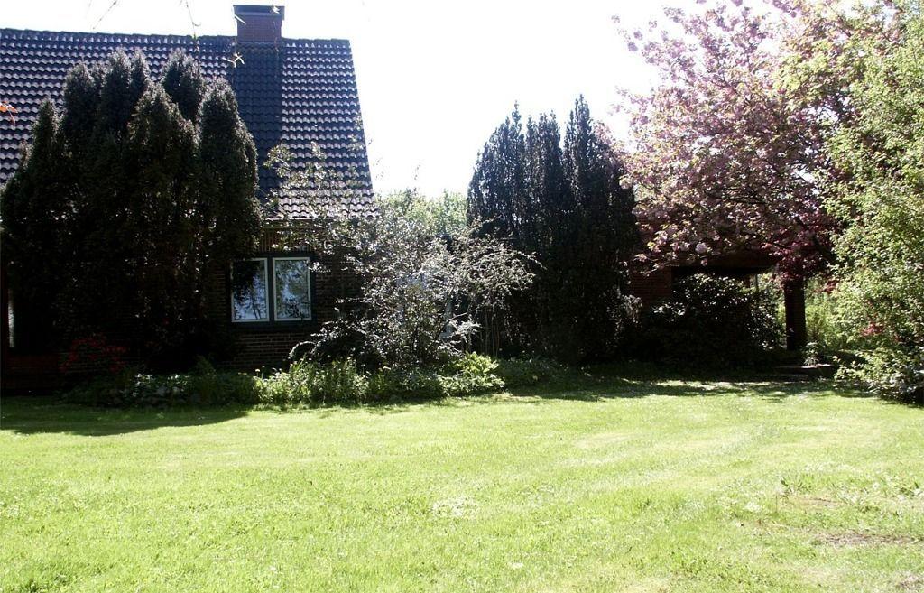 Haus mit Garten, Blumen und Bäumen im Hintergrund.