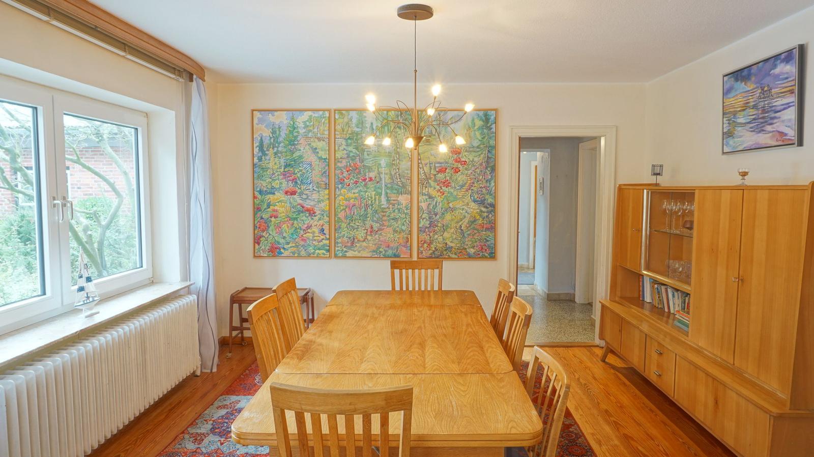 Esszimmer mit Holztisch, Stühlen und Wandbildern. Fenster und Holzfußboden.