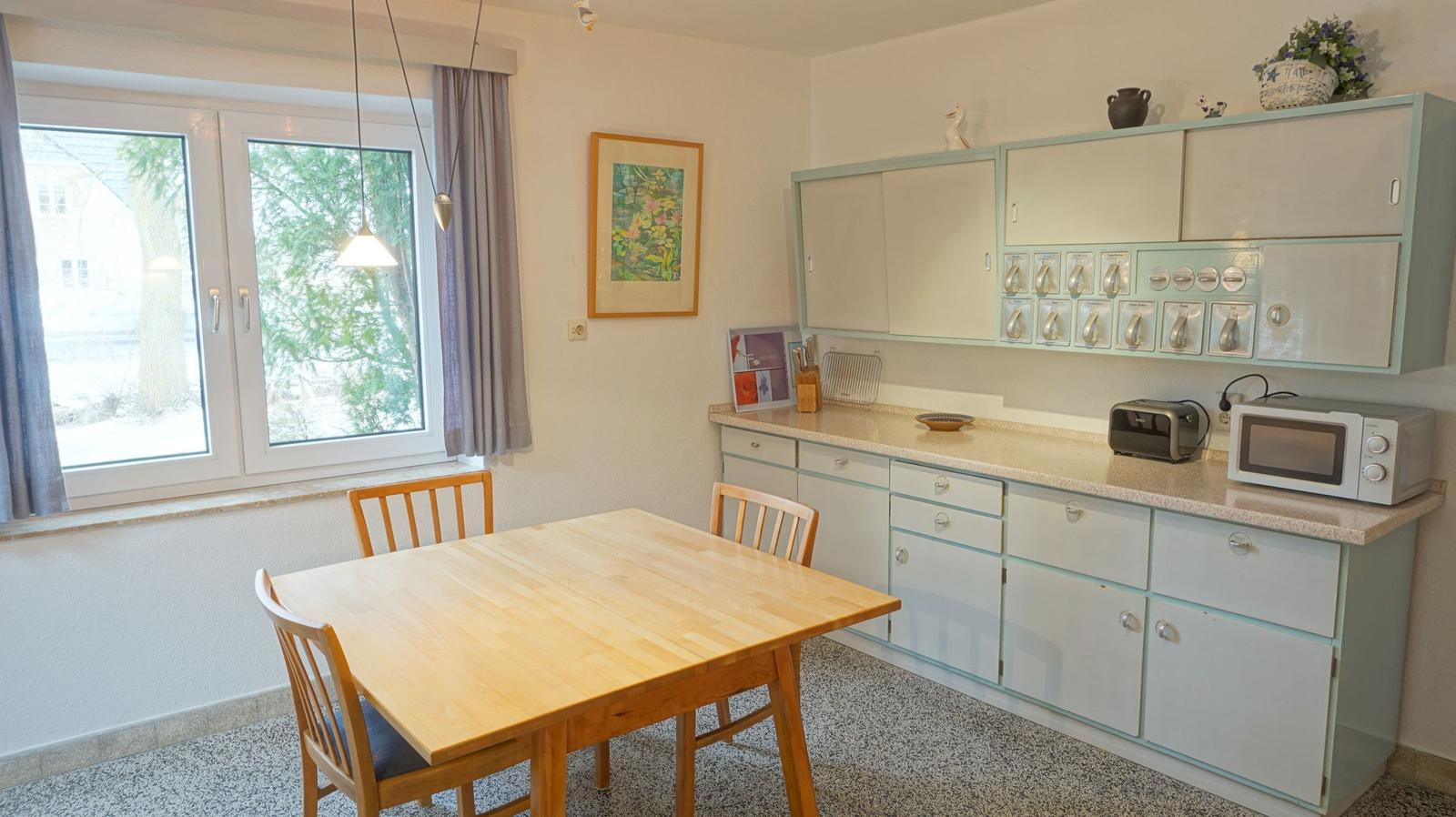 Küche mit Essbereich, Holztisch, Küchenzeile und Fenster.