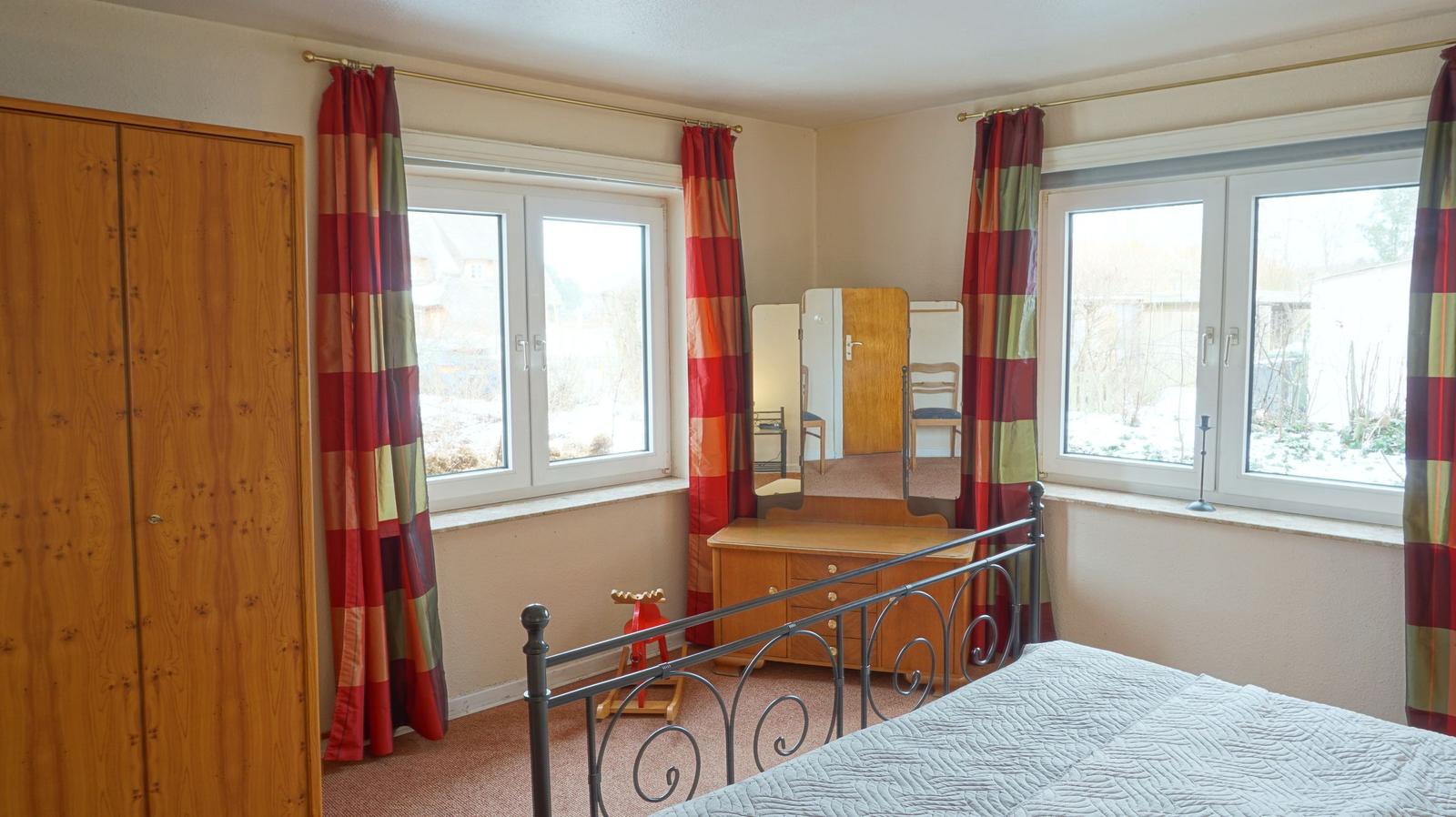 Schlafzimmer mit Bett, Kleiderschrank und Fenstern mit Vorhängen.