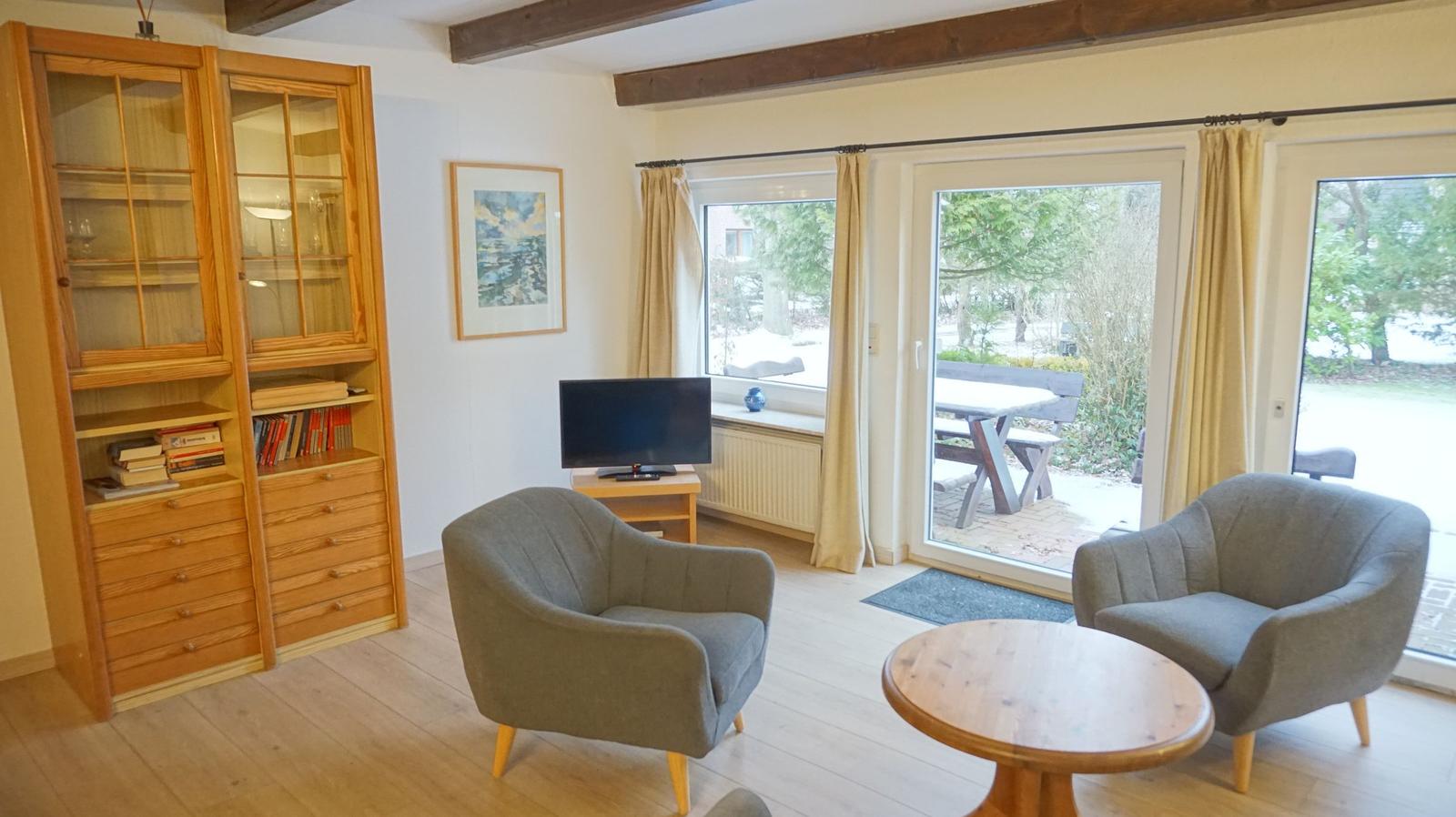 Wohnzimmer mit zwei Sesseln, Tisch, Fernseher und Glaswand zum Garten.