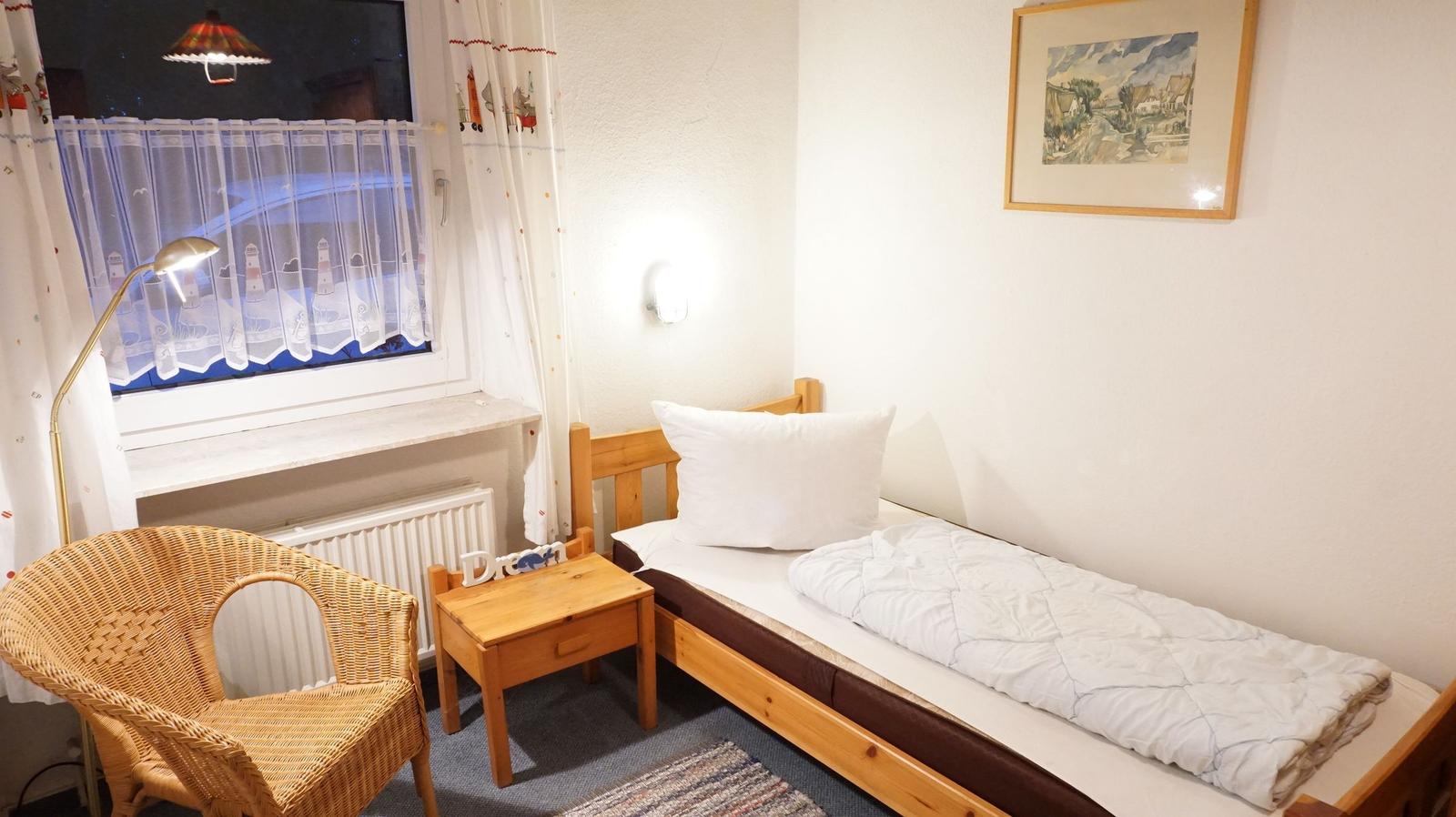 Ein Schlafzimmer mit Bett, Nachttisch, Stuhl und Fenster mit Vorhängen.