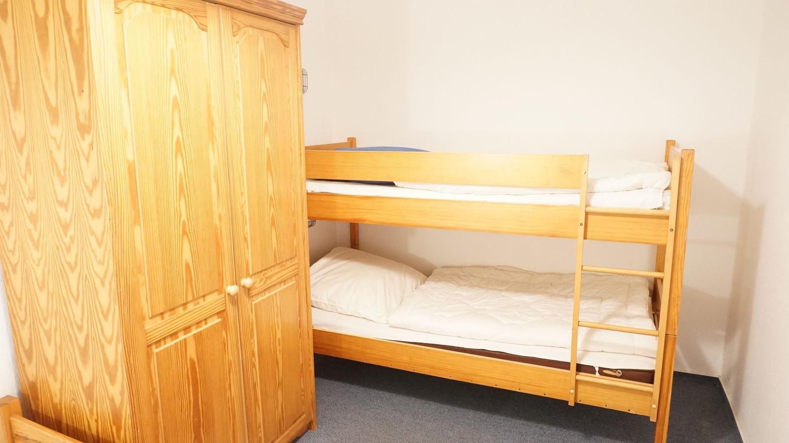 Zimmer mit Doppelstockbett und Holzschrank. Bettwäsche weiß.