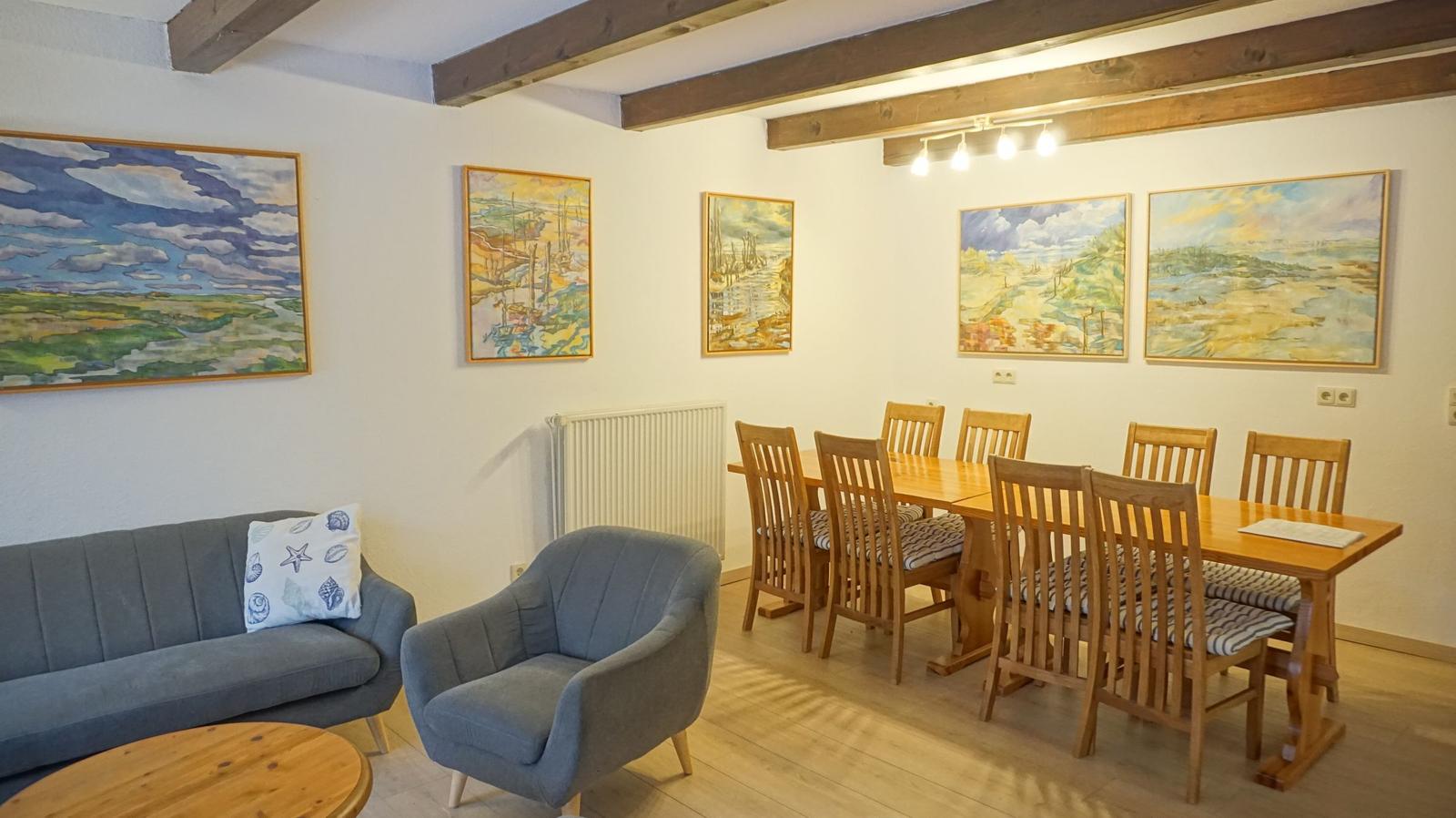 Wohn- und Essbereich mit Holzdecke, Sofa, Stuhl und Wandbildern.