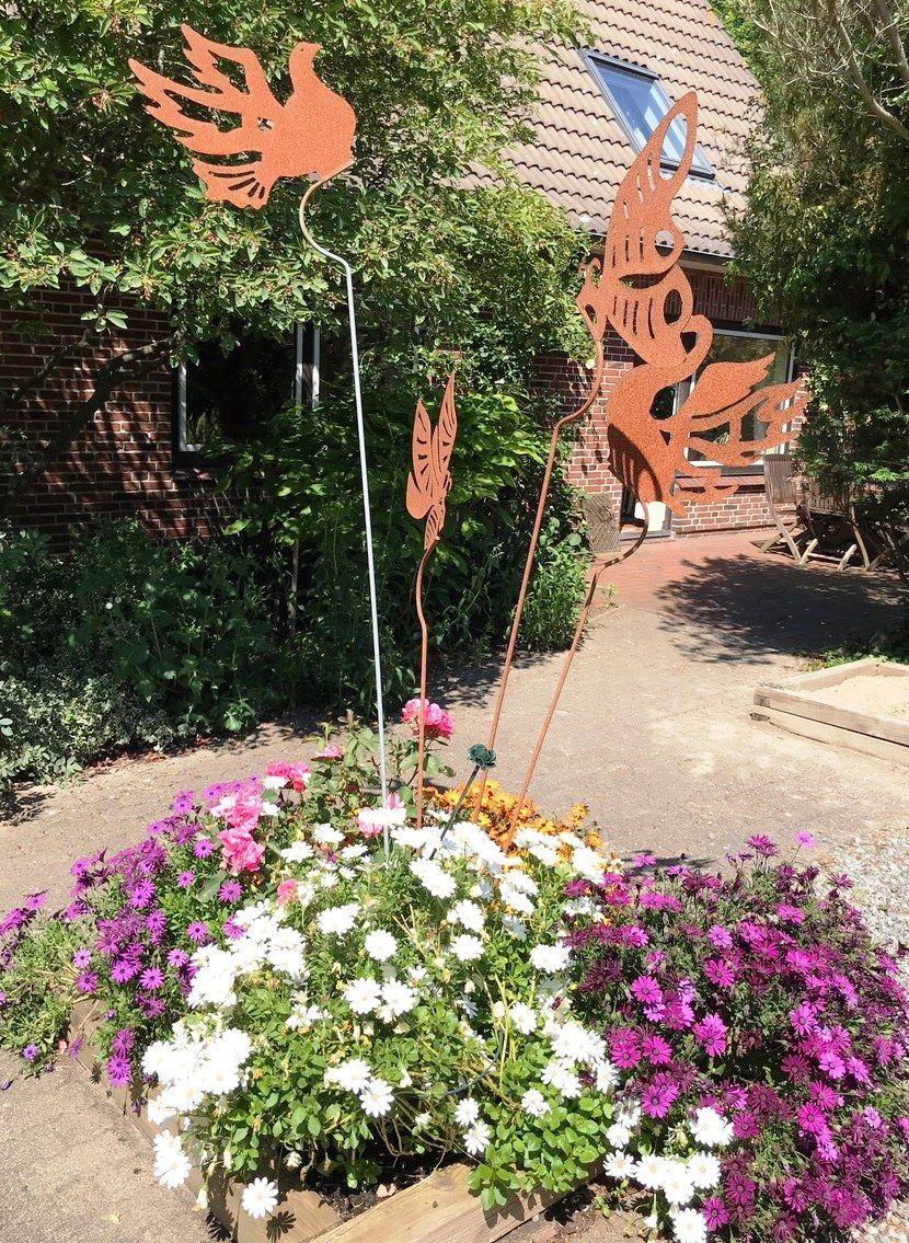 Garten mit Blumenbeete und Metallfiguren vor einem Haus.