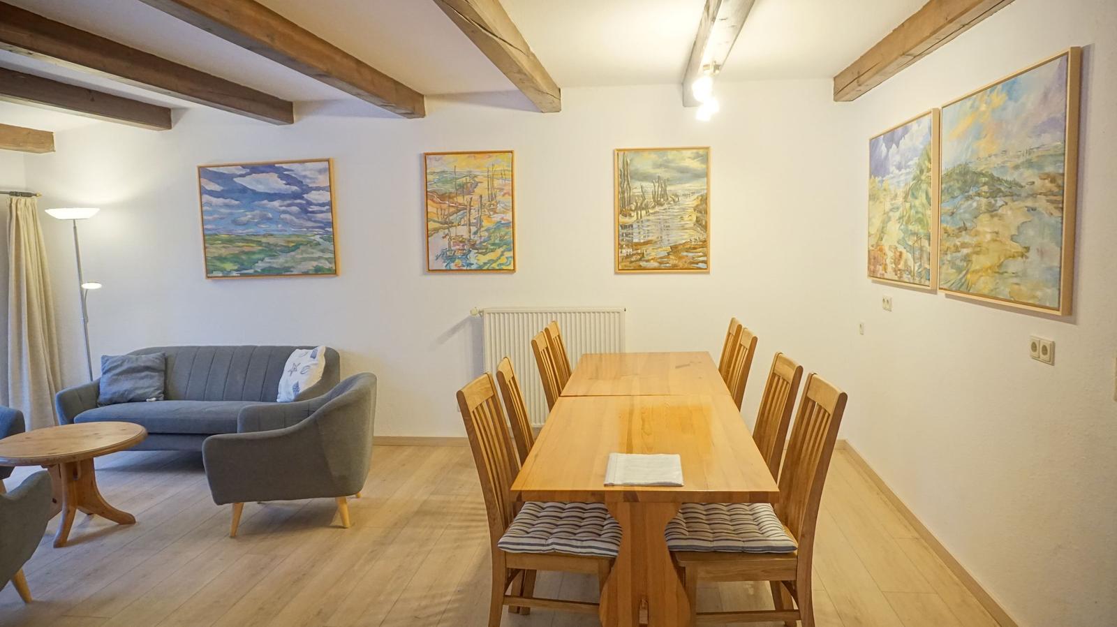 Wohn- und Essbereich mit Holzdecke, Sofa, Tisch und Wandgemälden.