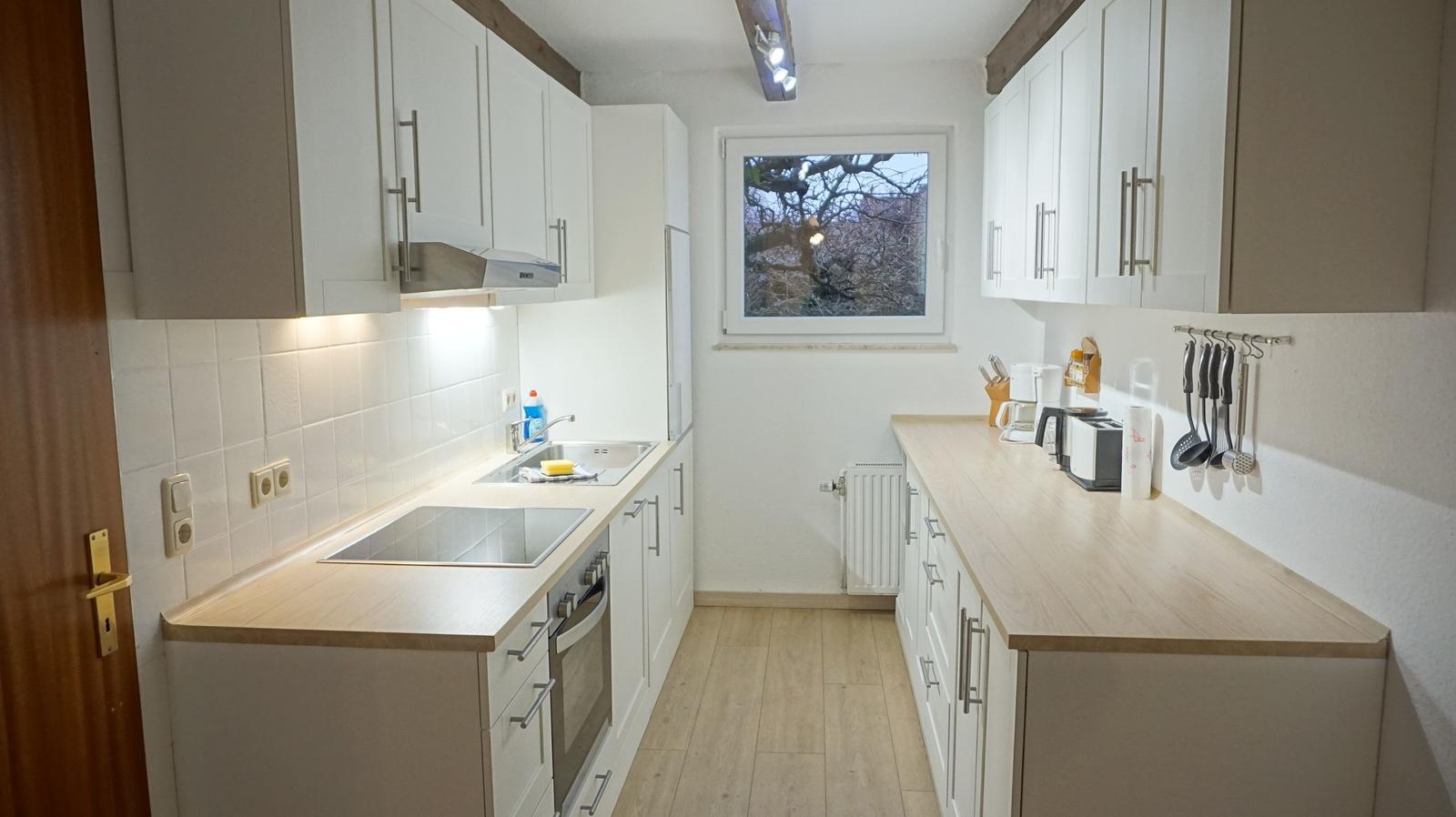 Küche mit weißen Schränken, Holzwerkzeug und Fenster.