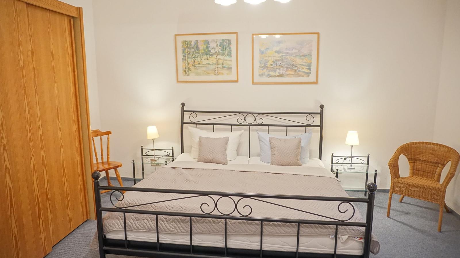 Schlafzimmer mit Bett, Nachttischen, Stühlen und Bildern an der Wand.