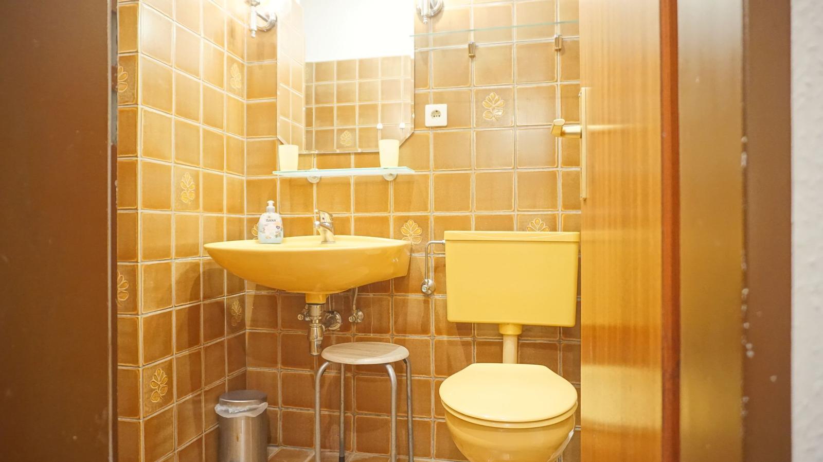 Badezimmer mit gelbem Waschbecken, Toilette und Spiegel an der Wand.