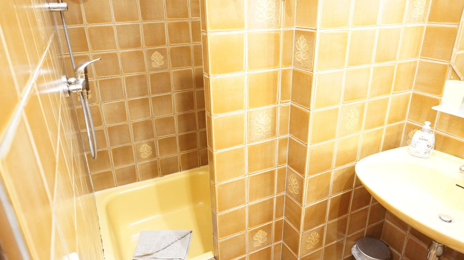 Bad mit Dusche, Waschbecken und gelben Fliesen