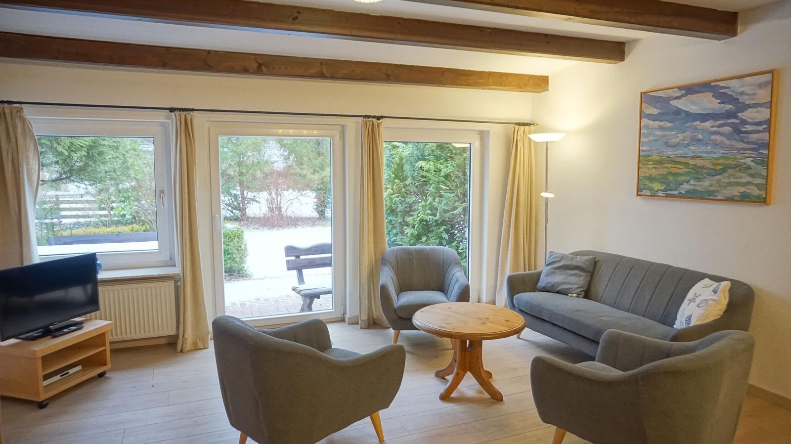 Wohnzimmer mit Sofa, Stühlen, Fernseher und Blick auf Garten.