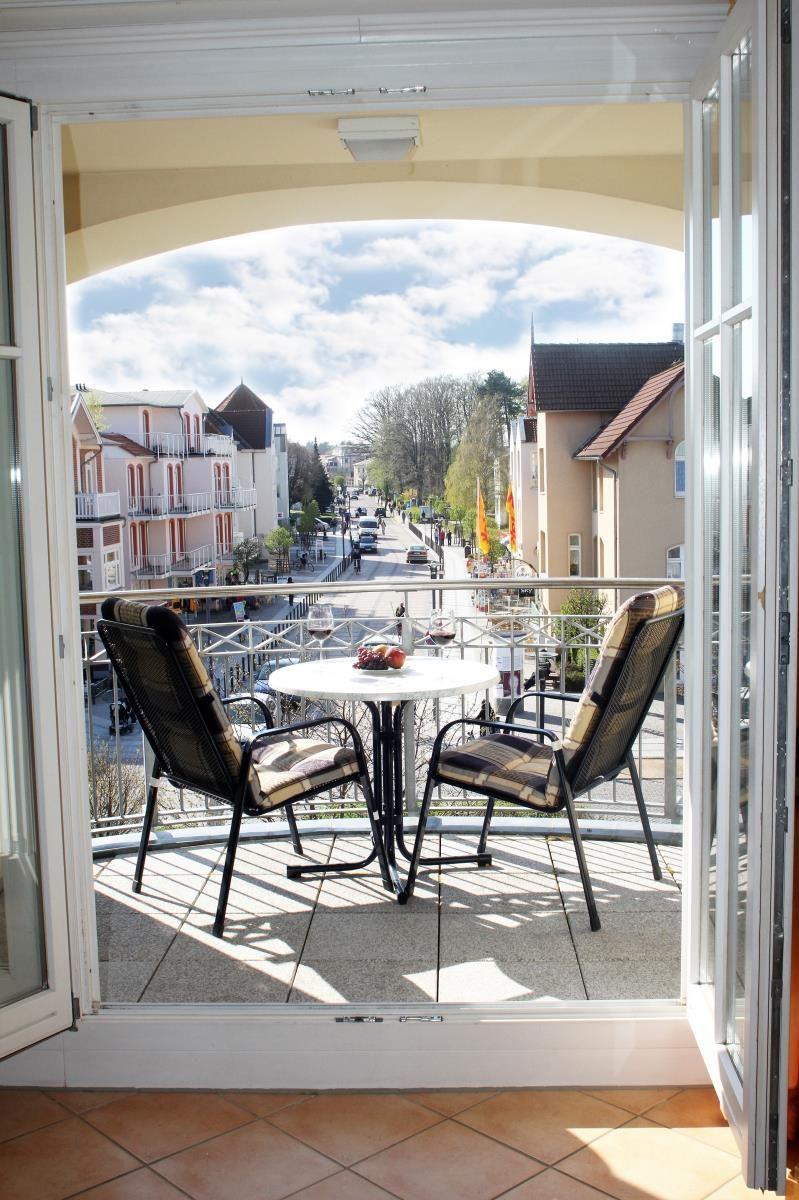 Balkon mit Tisch und zwei Stühlen. Blick auf eine Straße mit Gebäuden.