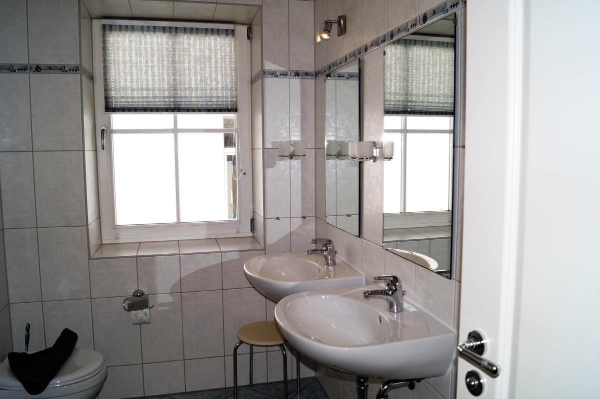 Badezimmer mit zwei Waschbecken, Spiegel und Fenster mit Rollladen.