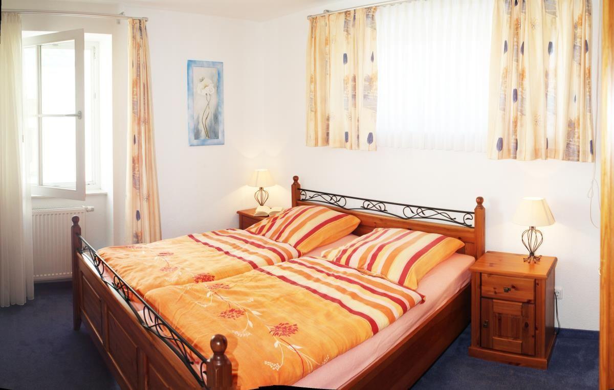 Schlafzimmer mit Doppelbett, zwei Nachttischen und Fenstern mit Vorhängen.
