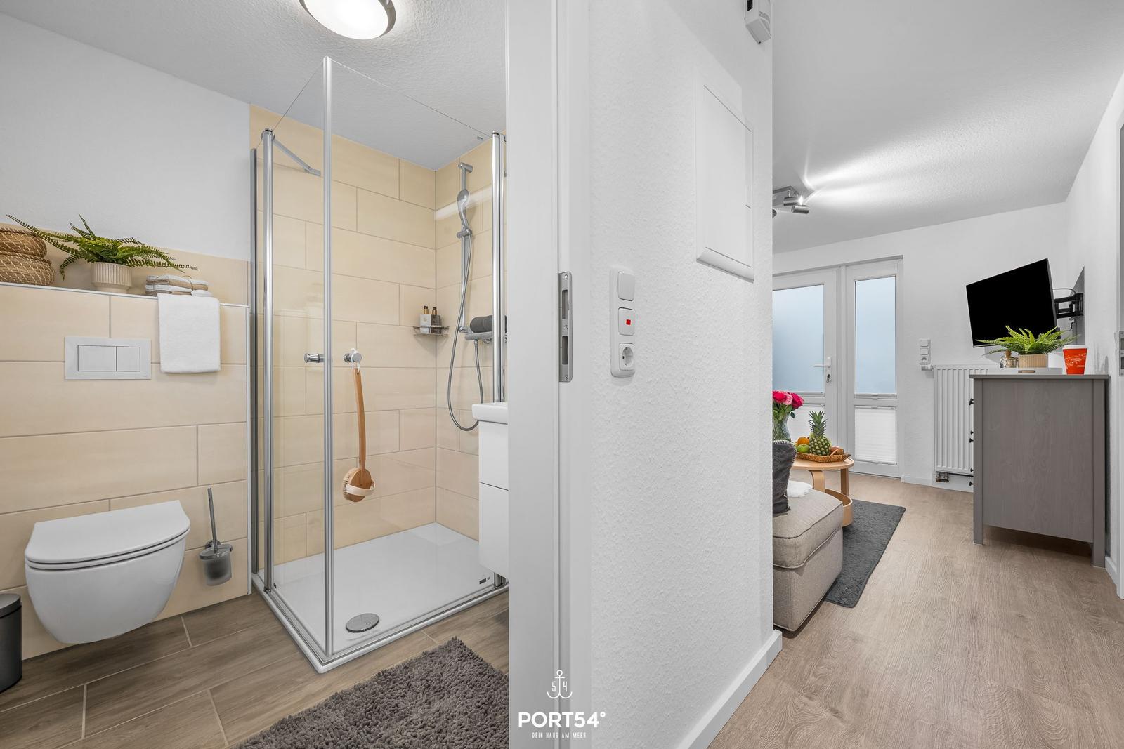 Badezimmer mit Dusche und Toilette. Wohnbereich mit TV und Sitzgelegenheit.