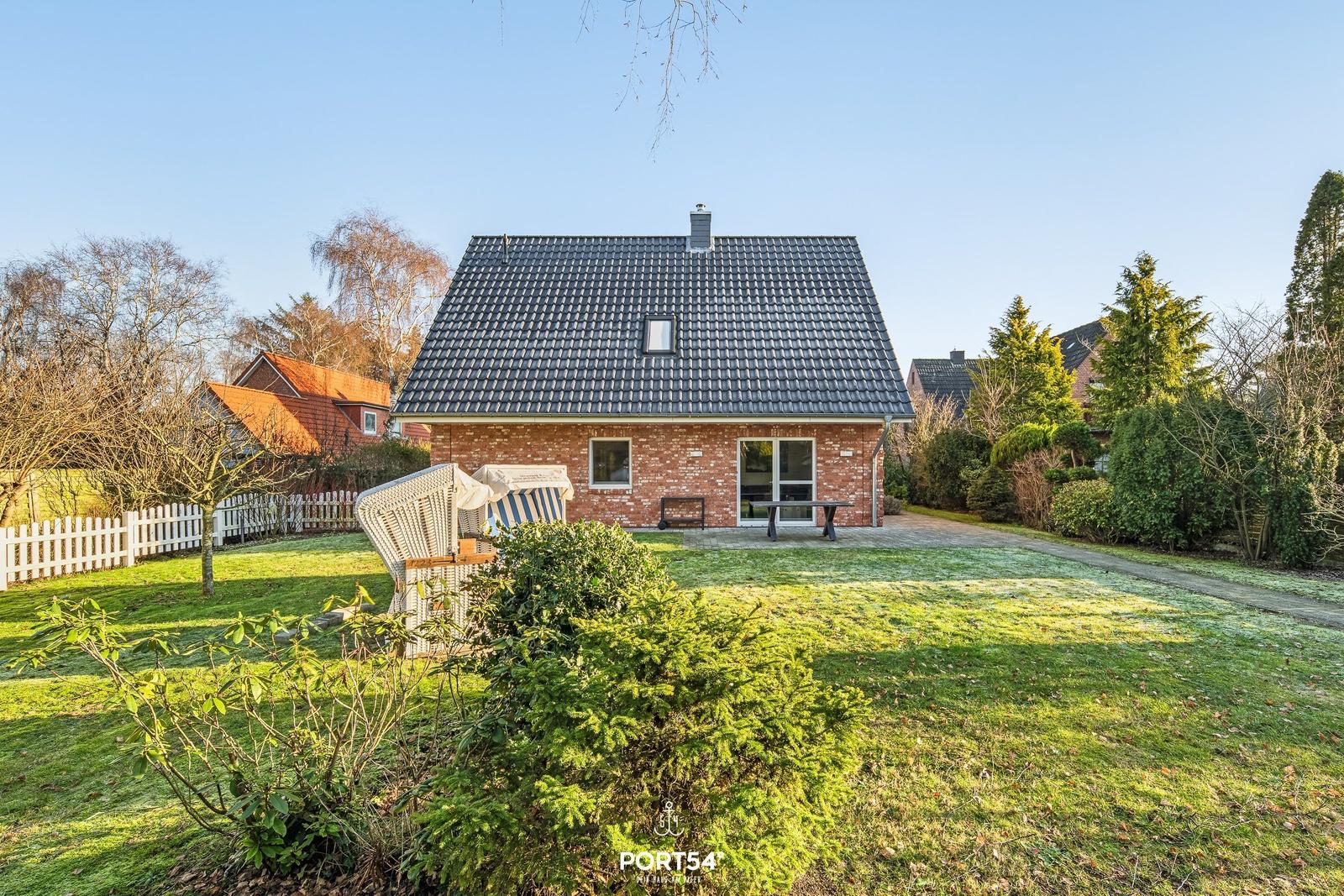 Ein Haus mit Garten, Terrasse und Gartenmöbeln unter klarem Himmel.