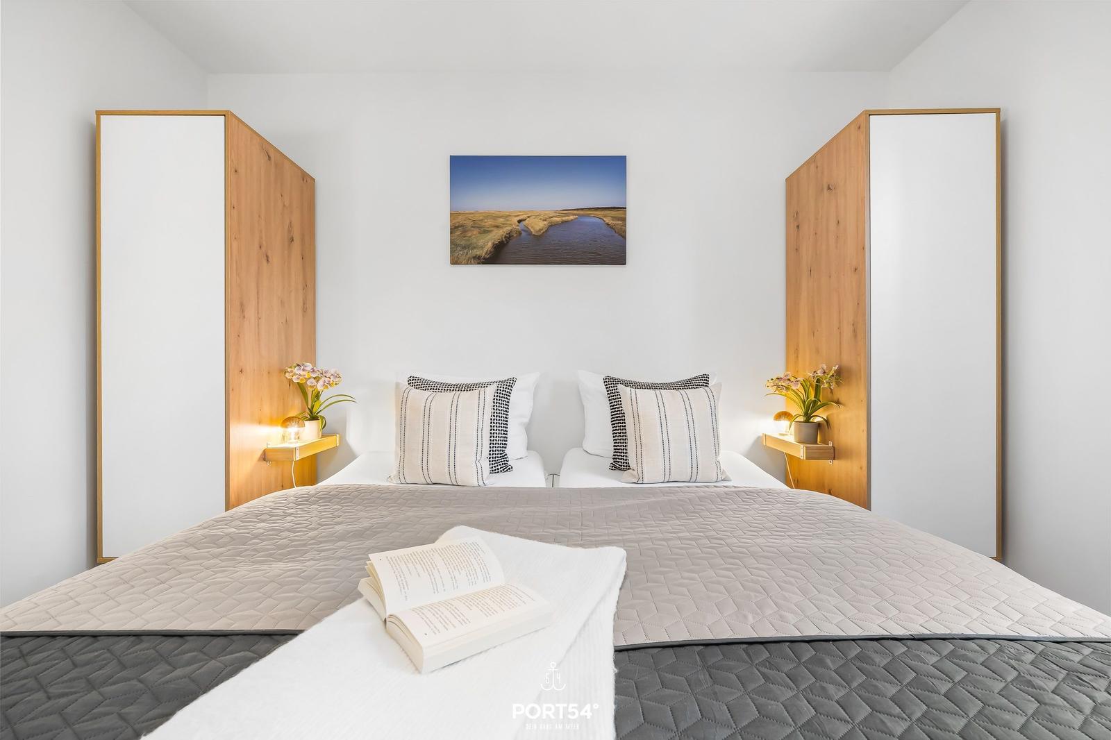 Schlafzimmer mit Bett, Kissen, Decke und Wandbild.