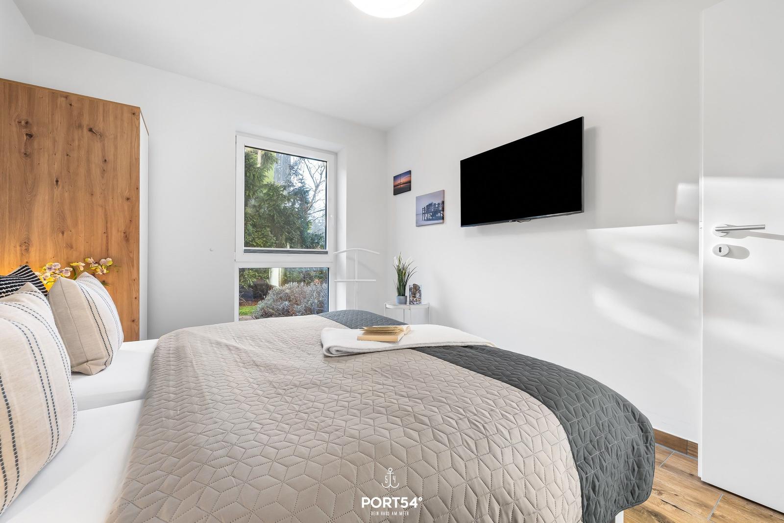 Schlafzimmer mit Bett, Fernseher und Fenster mit Blick auf Grün.