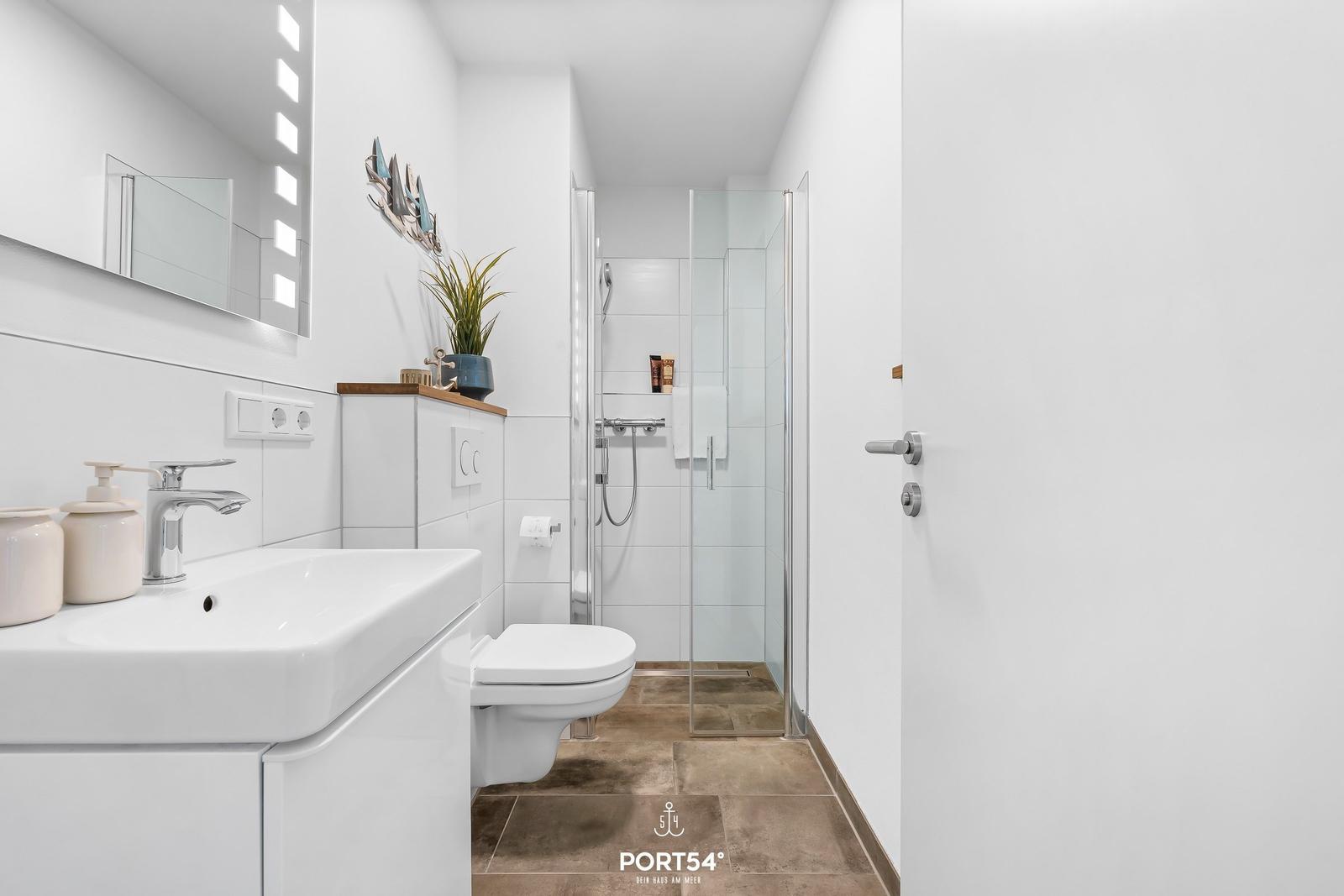 Badezimmer mit Dusche, Waschbecken und Toilette. Weiße Fliesen und Holzfliesen.