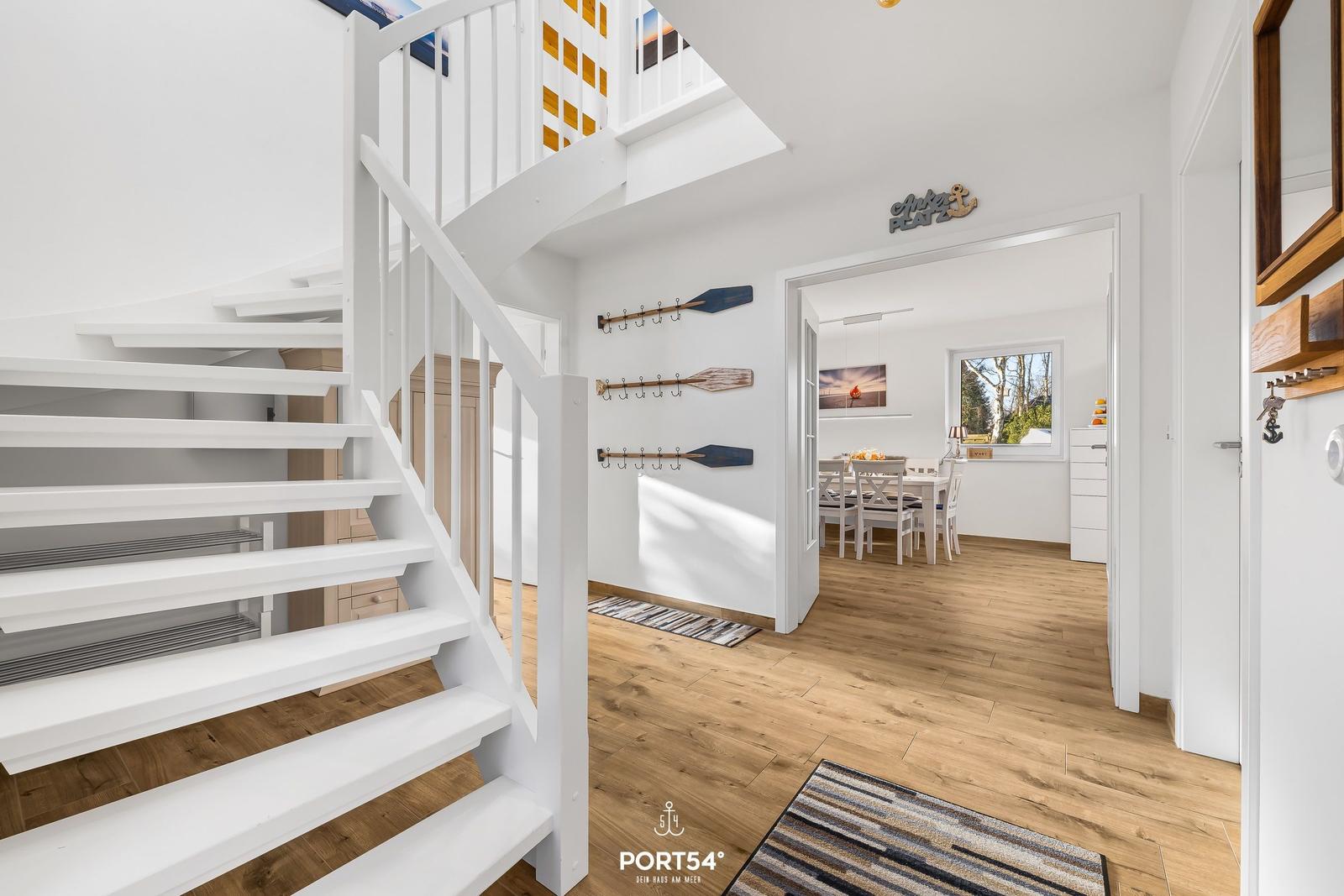 Haus mit weißer Treppe und Holzboden. Im Hintergrund ist Essbereich mit Tisch und Stühlen.
