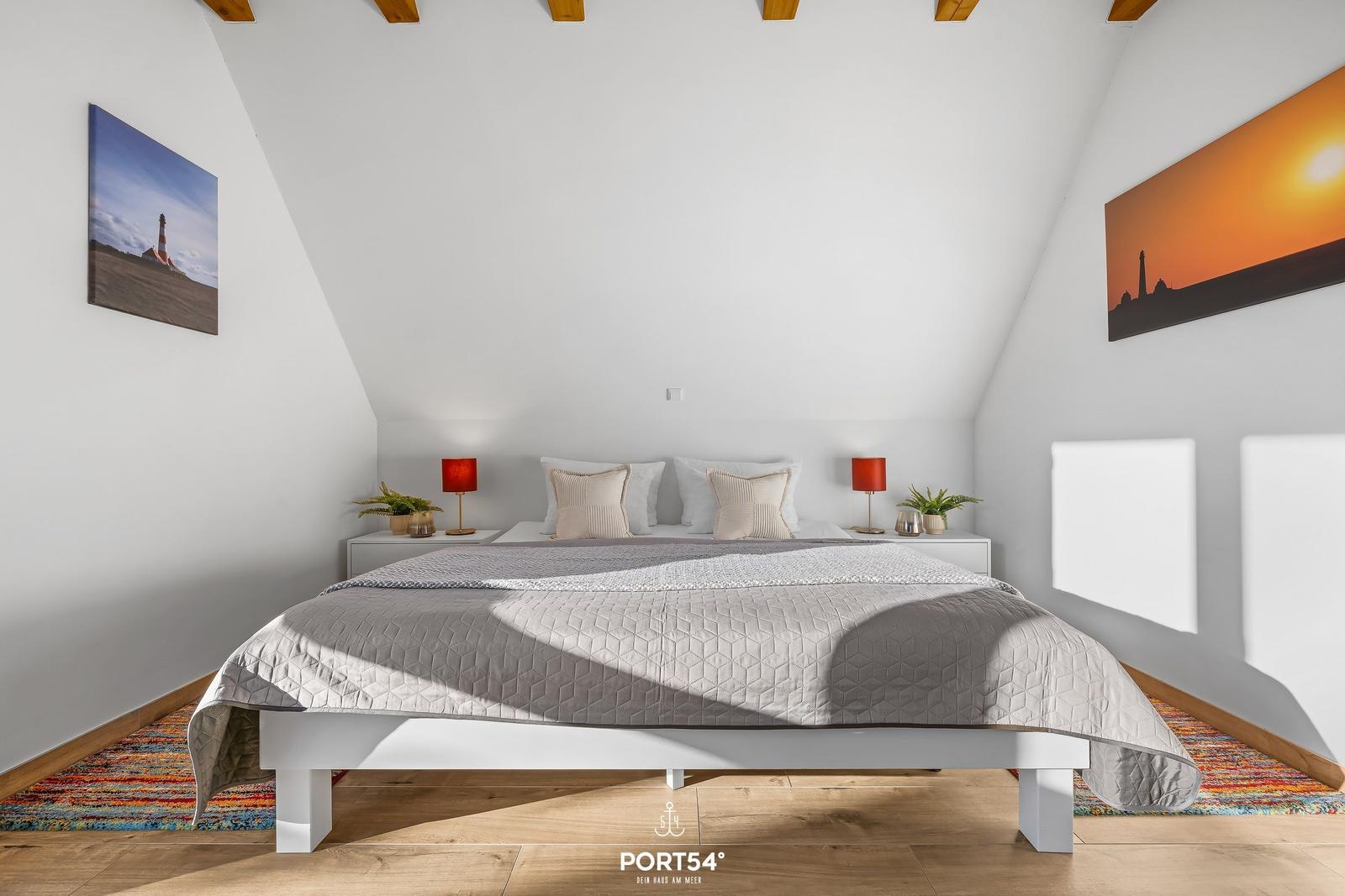 Schlafzimmer mit Dachschrägen, Bett, Nachttischen und Wandbildern.