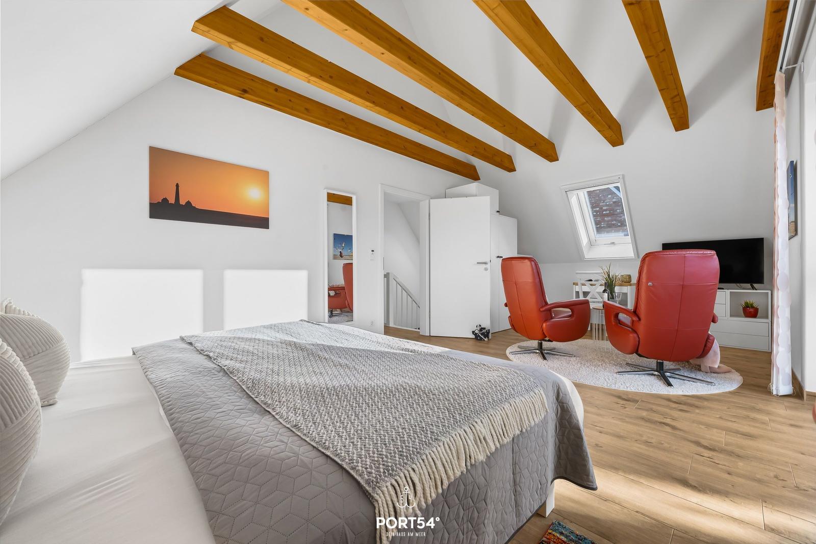 Schlafzimmer mit Dachschrägen, Bett, roten Sesseln und TV.