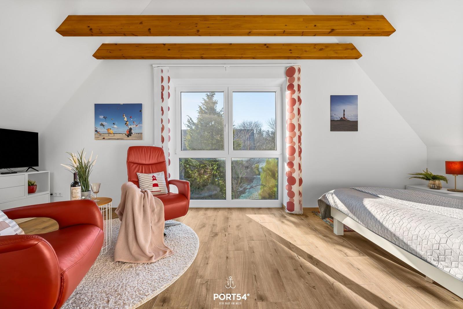 Schlafzimmer mit Blick auf die Landschaft, rotem Sessel und Bett.