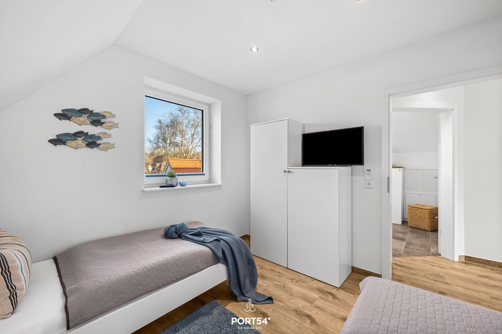 Zimmer mit zwei Betten, Fenster und TV-Schrank. Blick auf Dachziegel.