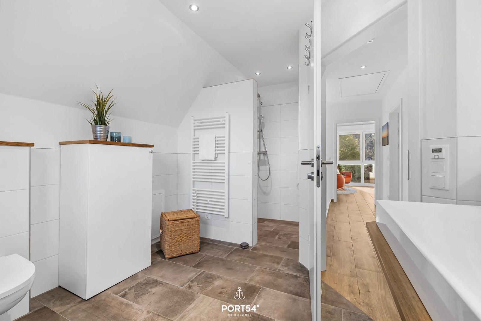 Badezimmer mit Dusche, Badewanne und Toilette. Holzboden und weiße Fliesen.