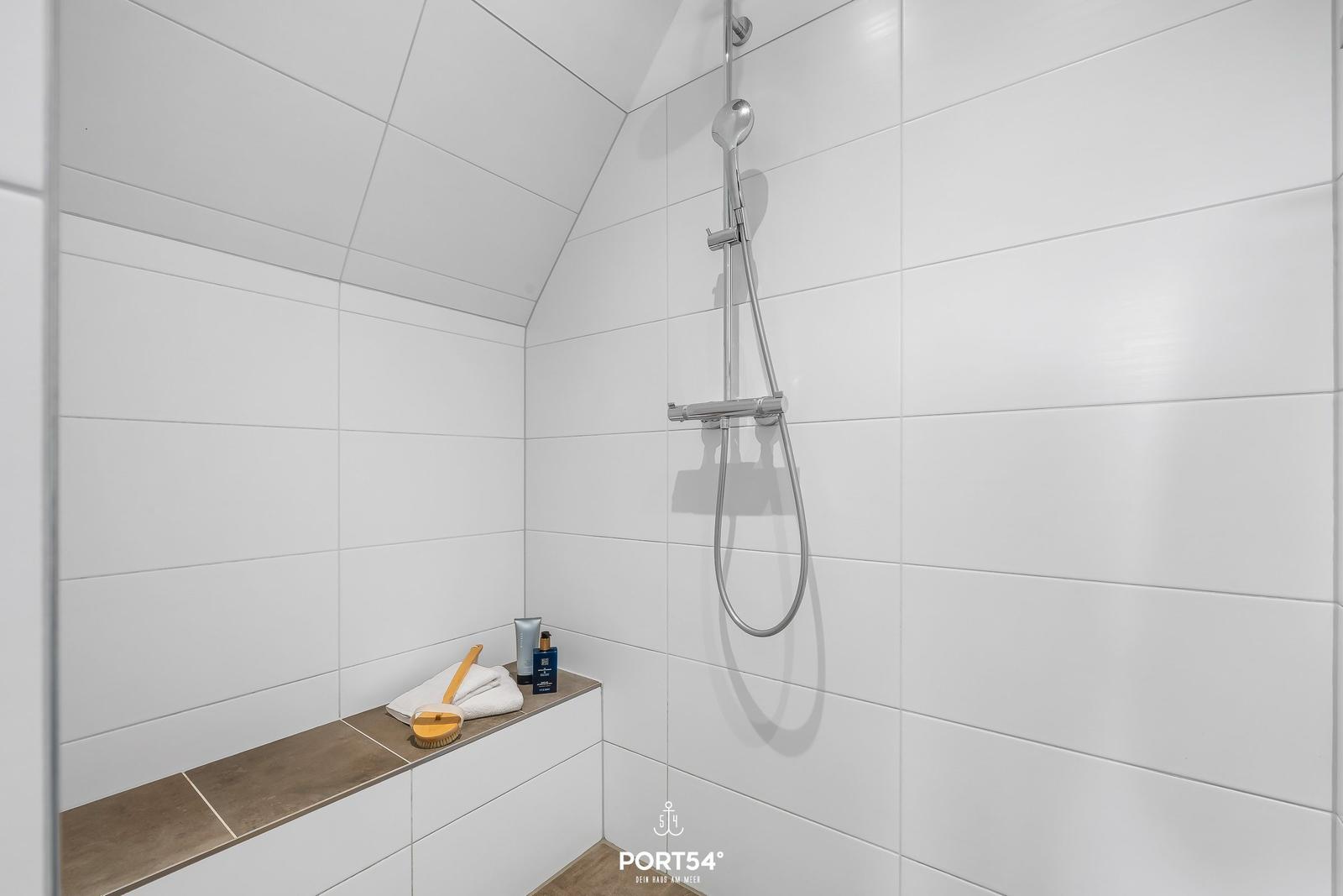 Duschkabine mit Duschbrause, Handtuch und Pflegeprodukten auf Sitzbank.