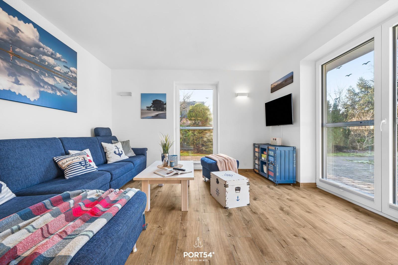 Wohnzimmer mit blauem Sofa, Holzboden und großen Fenstern.