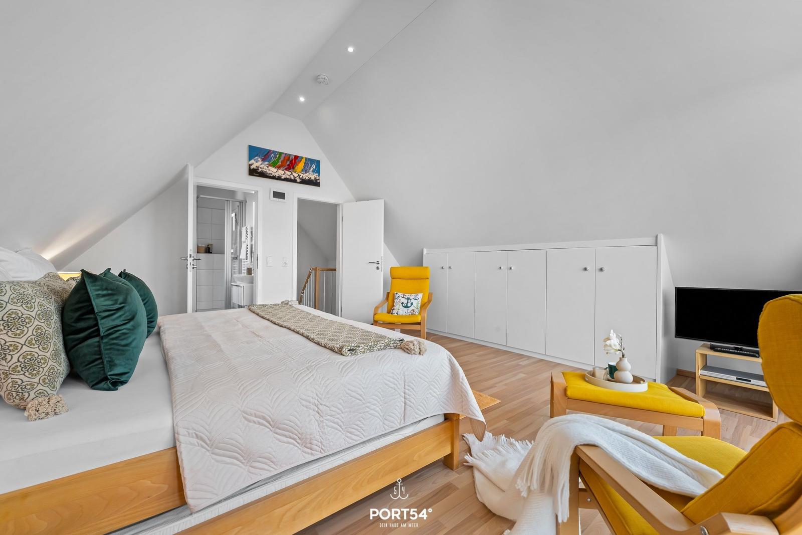 Schlafzimmer mit Dachschrägen, Bett, gelben Sesseln und weißen Schränken.