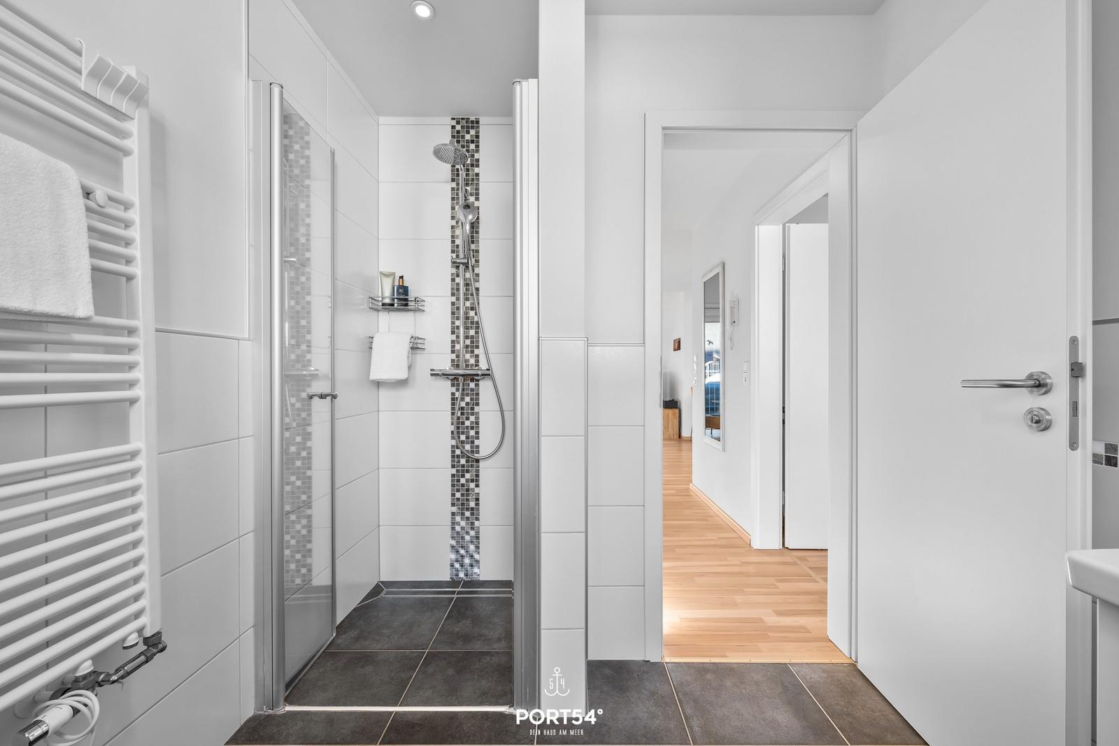 Badezimmer mit Dusche, Heizkörper und Blick in den Flur.