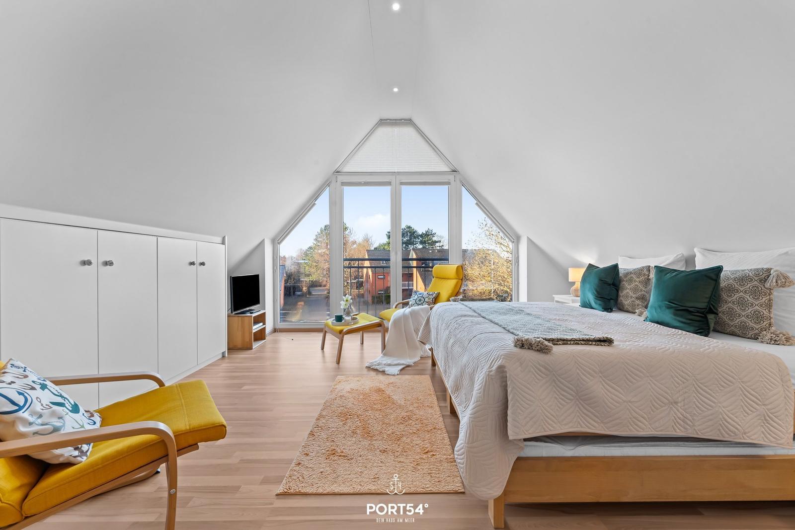 Schlafzimmer mit großem Bett, gelben Sesseln und großem Fenster zur Terrasse.