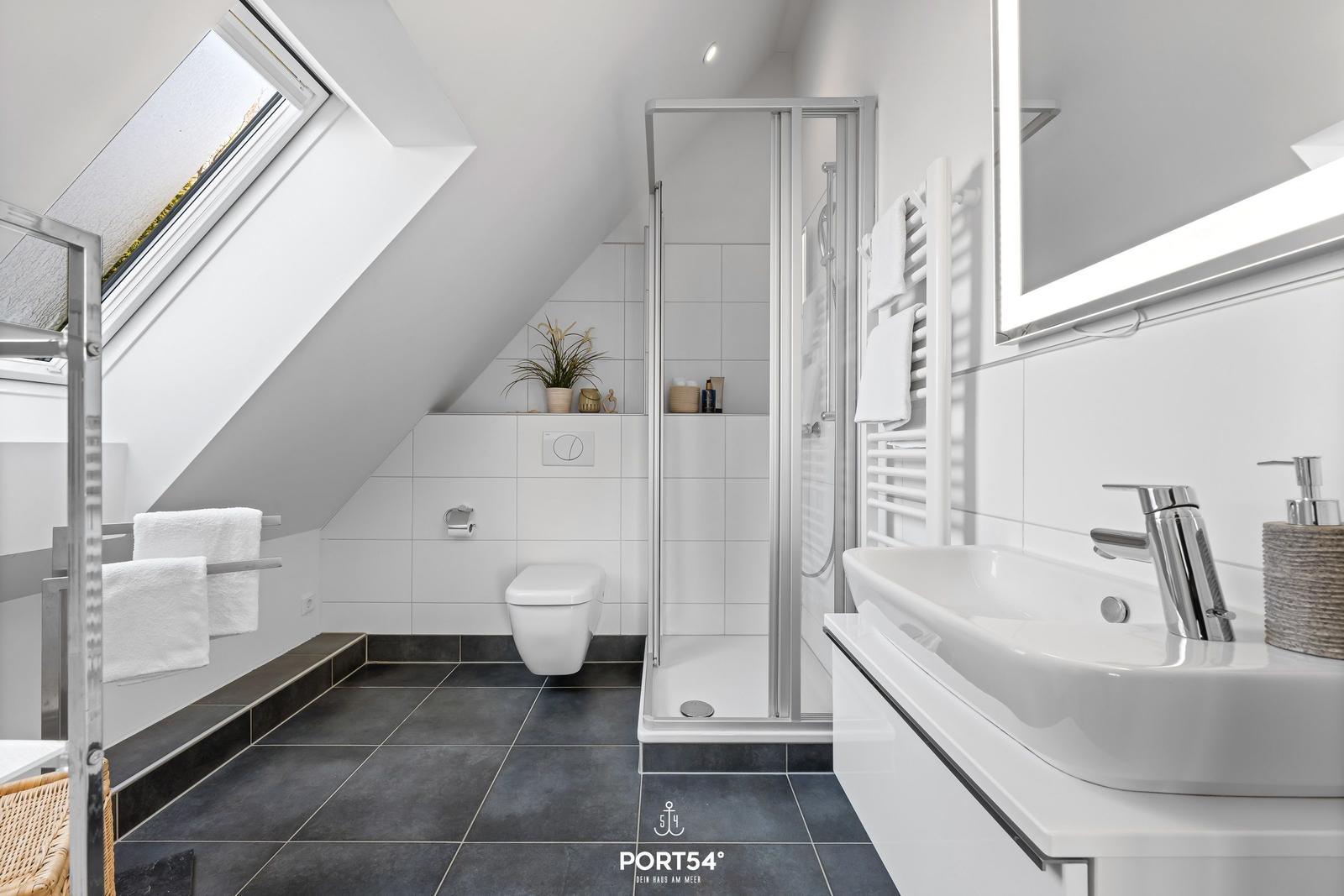 Badezimmer mit Dusche, Waschbecken und Toilette unter Dachschrägen.