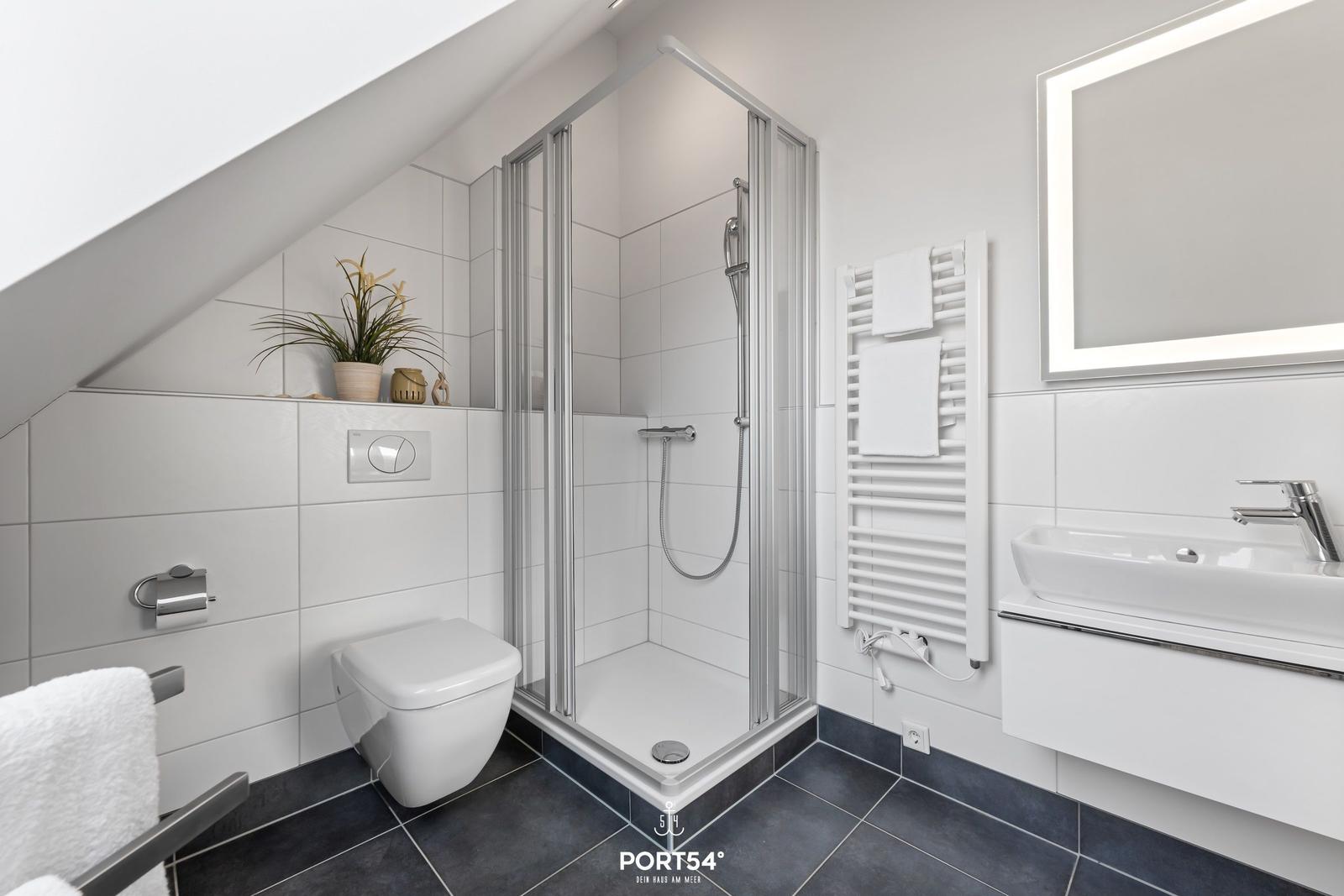 Badezimmer mit Dusche, Waschbecken und Toilette unter Dachschräge