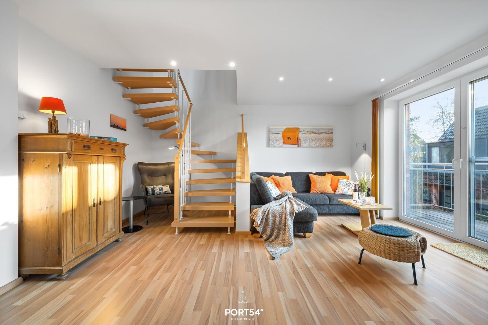 Wohnraum mit Holzdielen, Sofa, Treppe und Balkontür.