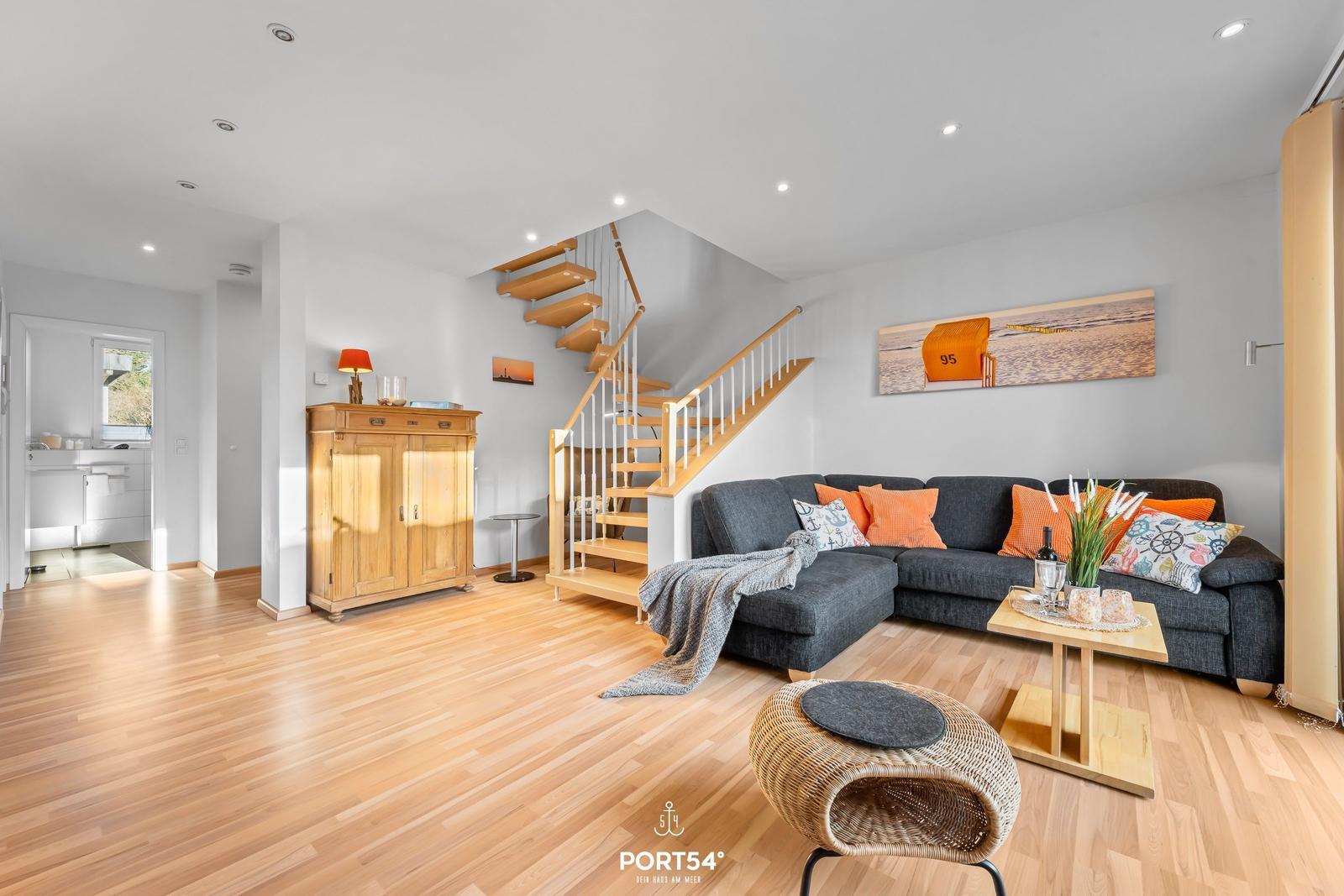 Wohnzimmer mit Sofa, Tisch und Treppe. Holzboden und Wandbild mit Strandmotiv.