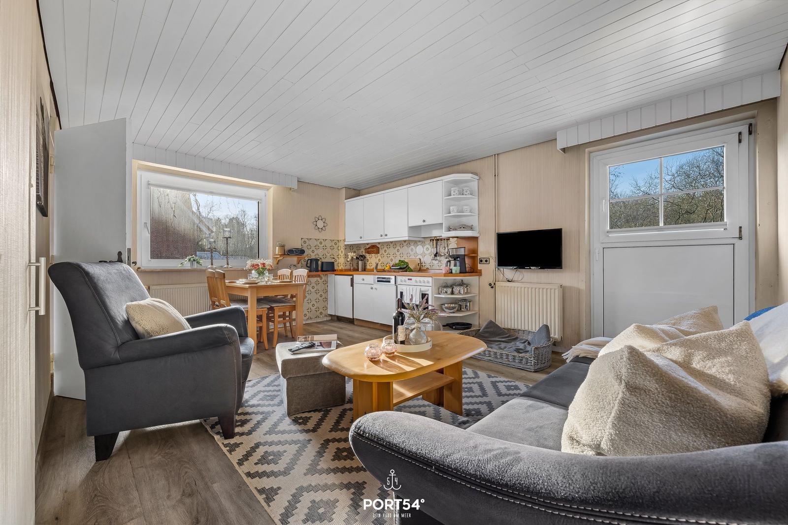 Wohn- und Küchenbereich mit Essplatz, Sofa, Sessel und TV.