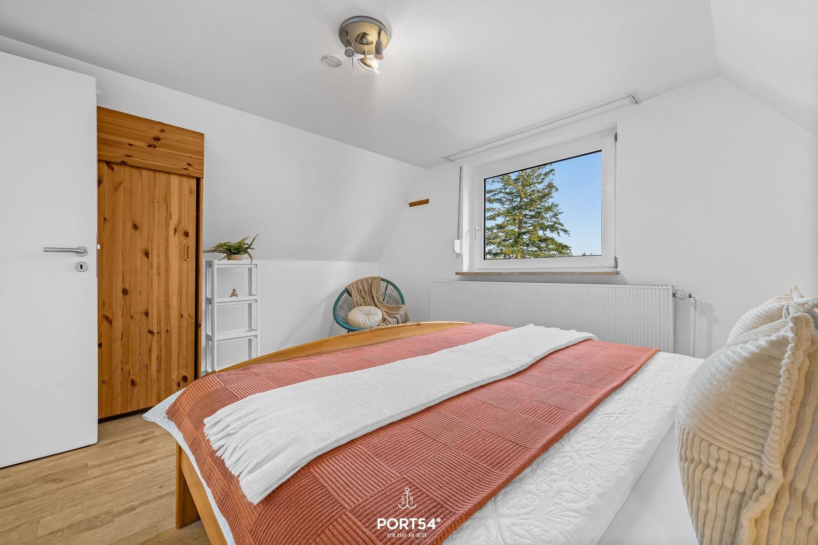 Schlafzimmer mit Bett, Fenster und Holztür.