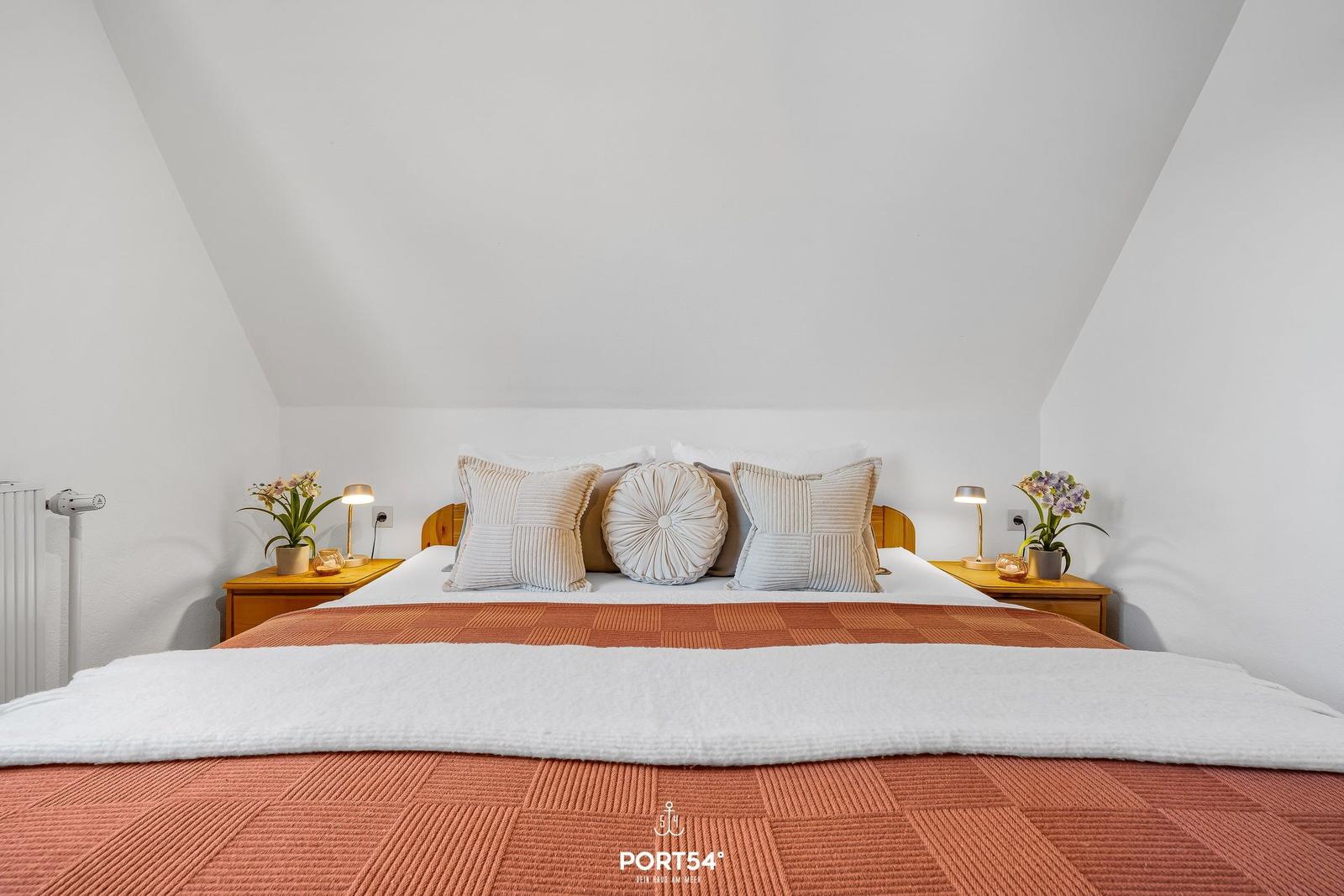 Schlafzimmer mit Bett, Nachttischen und Blumen.