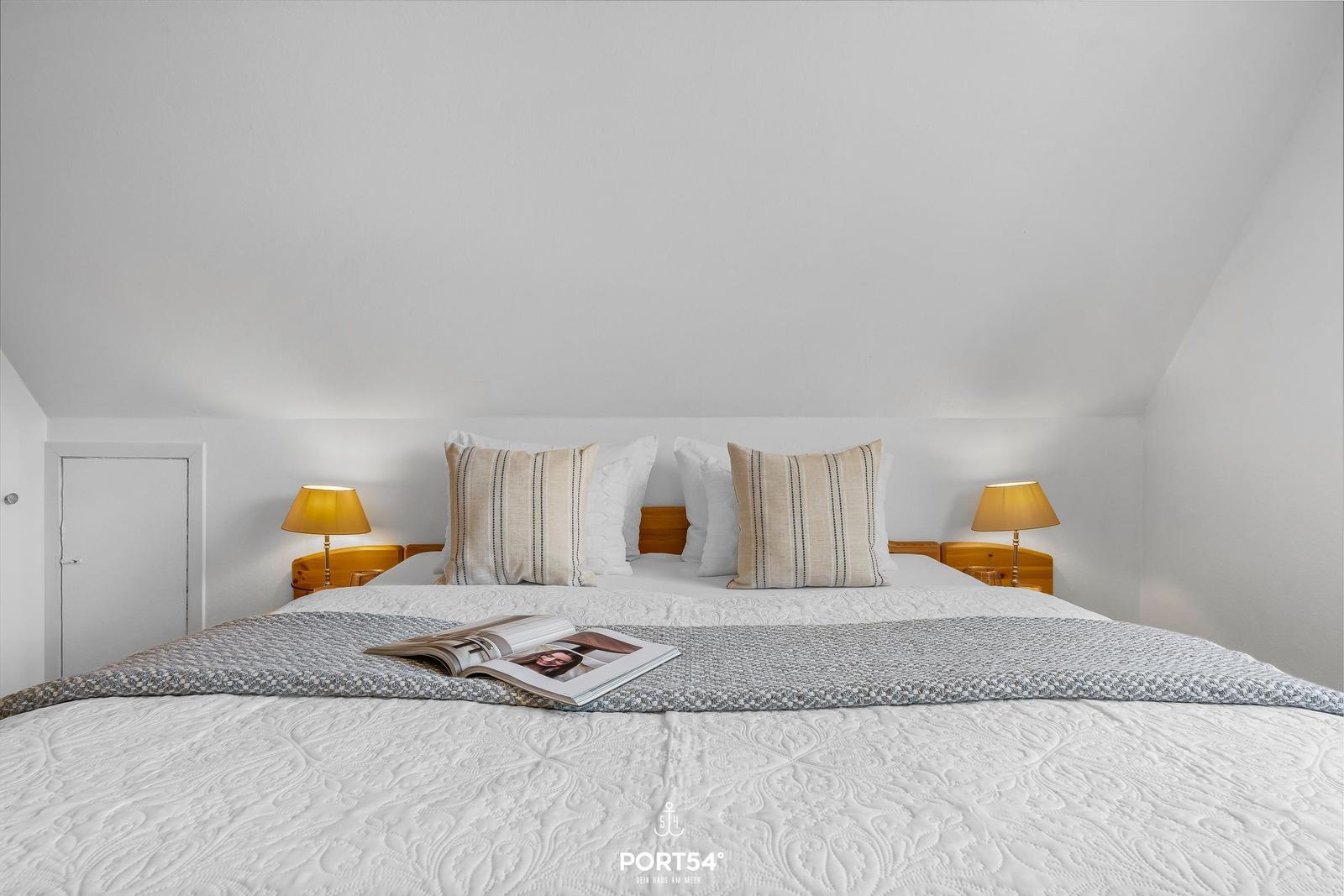 Doppelbett mit Kissen und Bettwäsche, zwei Nachttische mit Lampen, Tür links