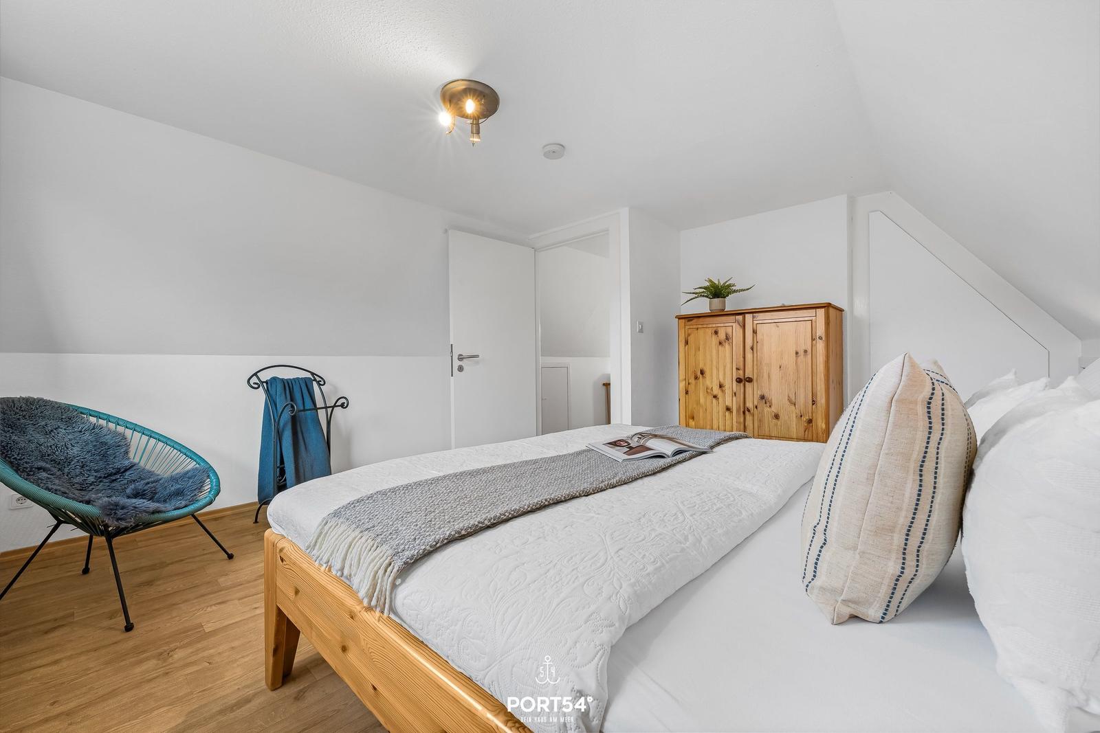 Schlafzimmer mit Holzbett, Kleiderschrank und Sessel.