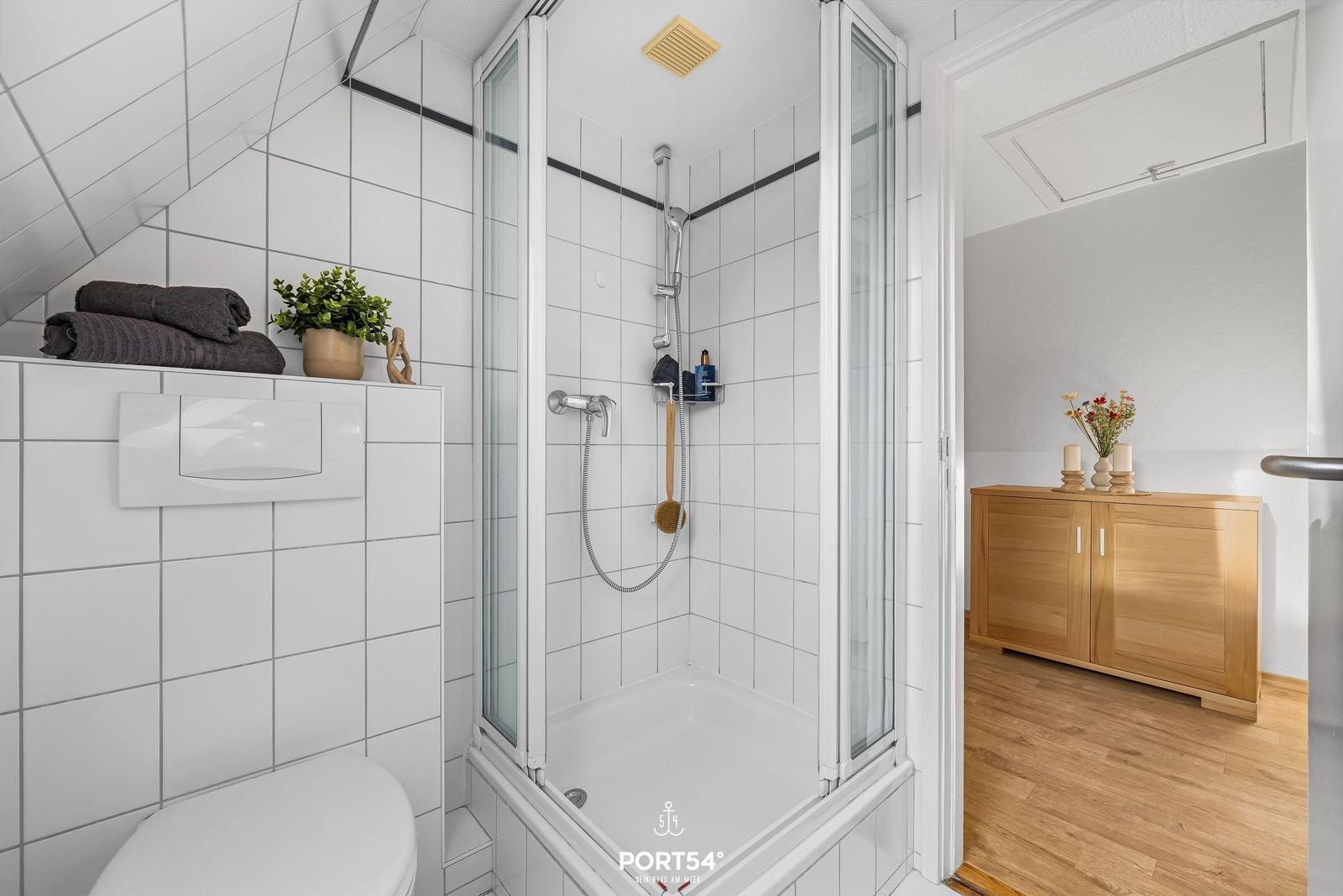 Badezimmer mit Dusche, Toilette und Holzschrank im Flur.