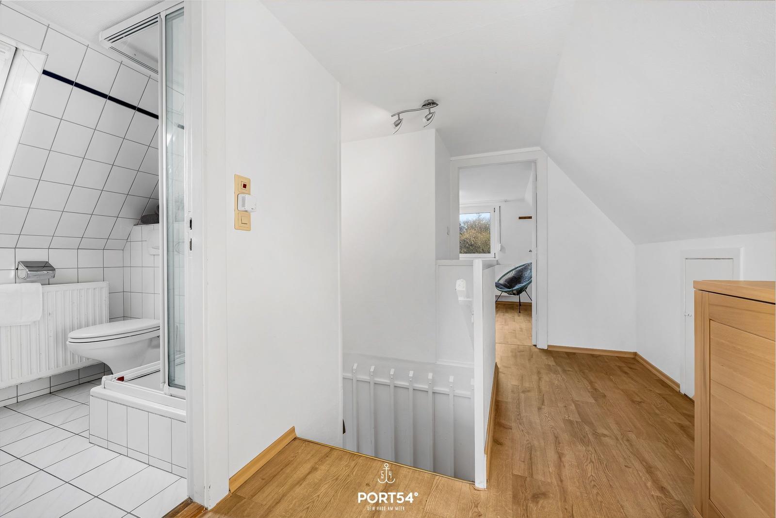 Badezimmer mit Dusche und Toilette. Holzfußboden und Schlafzimmer im Hintergrund.