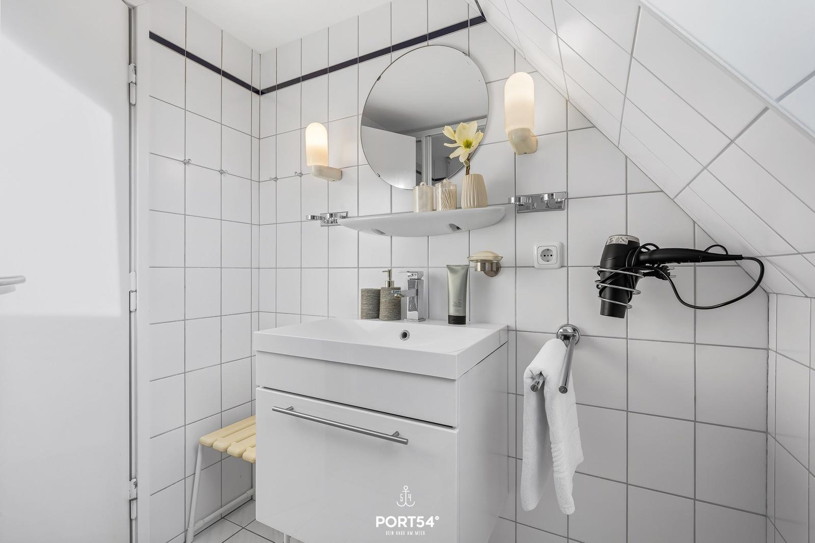 Badezimmer mit Waschbecken, Spiegel und Handtuchhalter an schräger Wand.