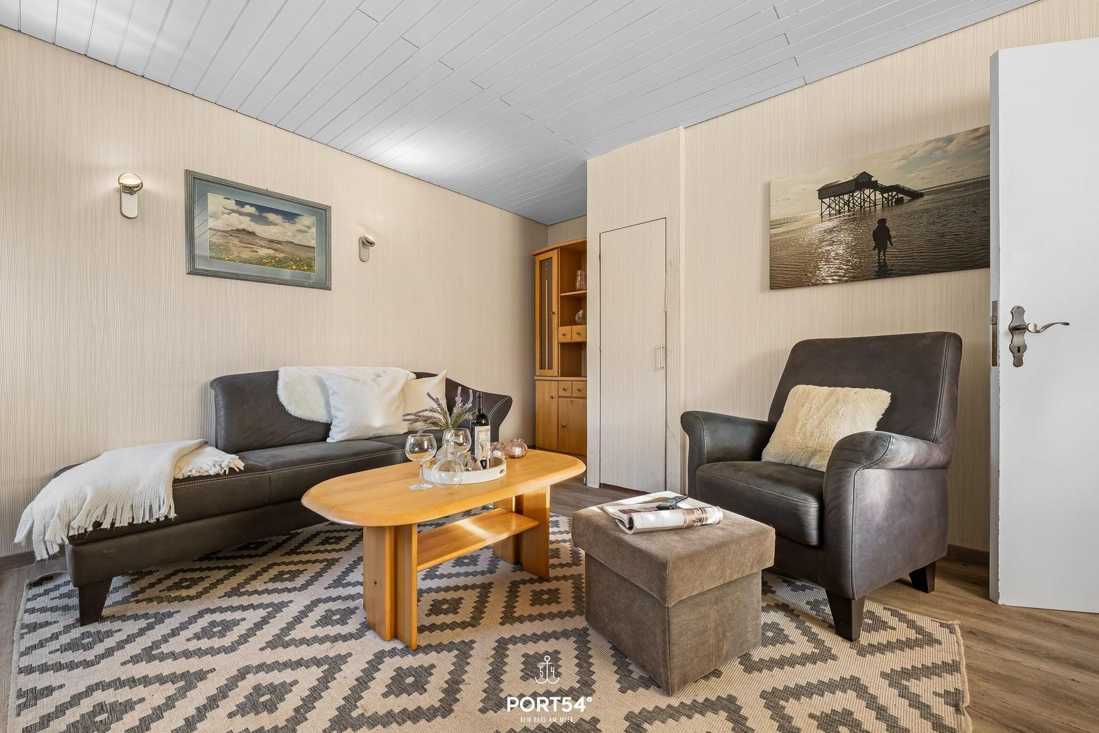 Wohnzimmer mit Sofa, Sessel und Holztisch auf Teppich