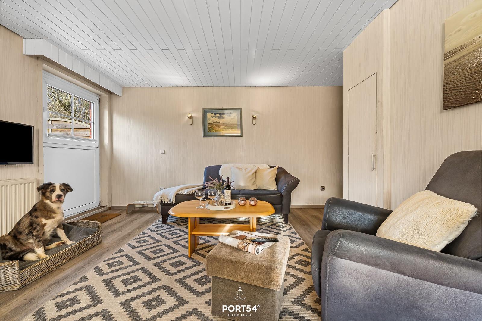 Wohnzimmer mit Sofa, Sessel, Couchtisch und Hund.