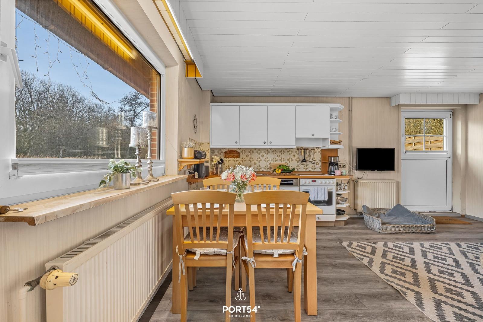 Küche mit Esstisch, Fenster und TV. Holzfußboden und weiße Schränke.